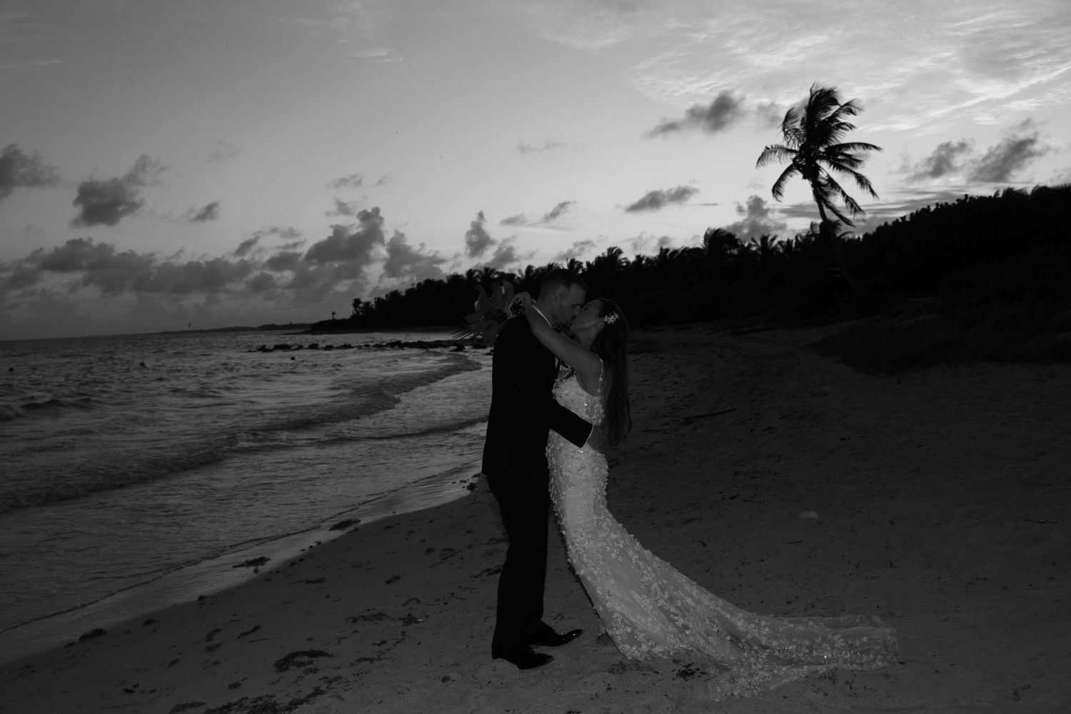 Dramatic beach wedding silhouettes captured during golden hour with waves crashing in the background.