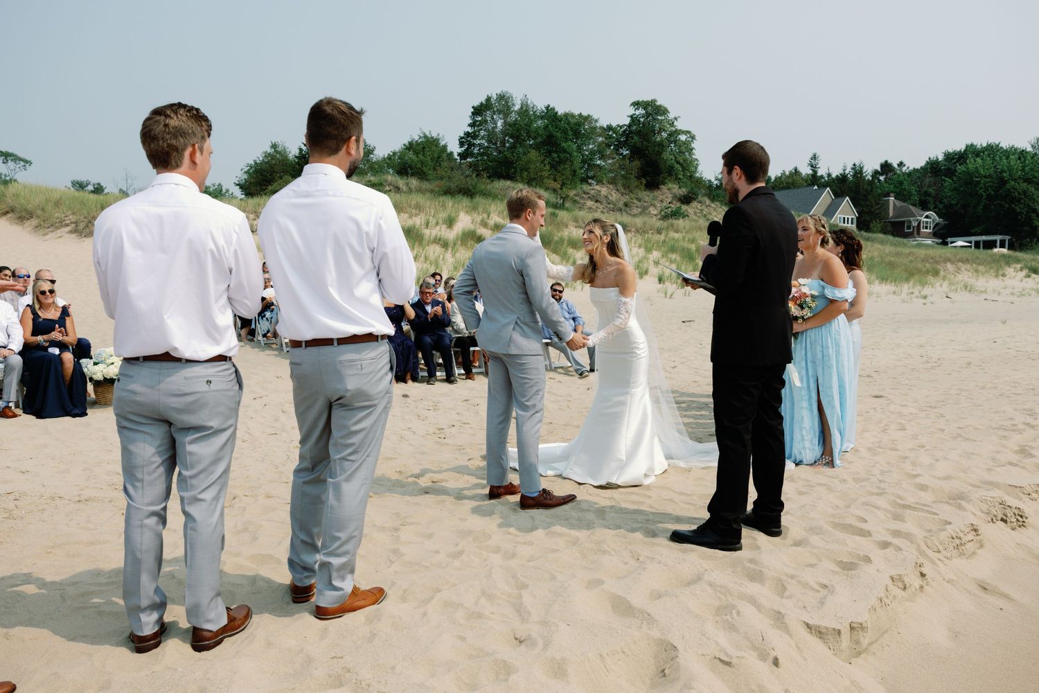 Wedding guests gathered on beach sand during outdoor ceremony.