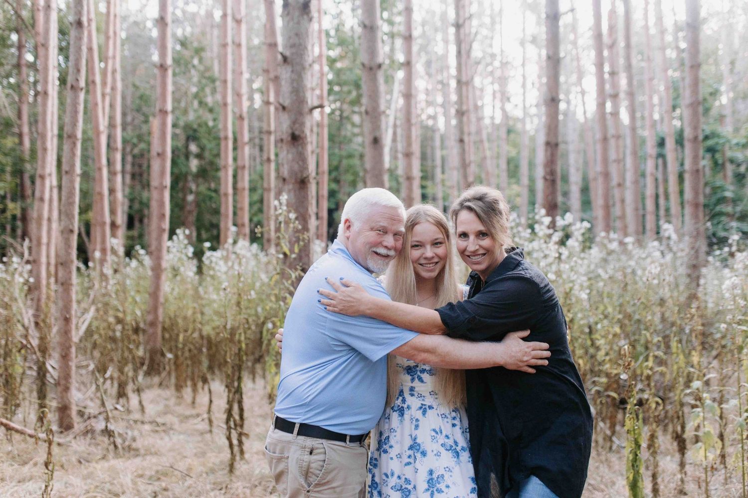 A group poses together in a pine forest setting wearing casual attire.