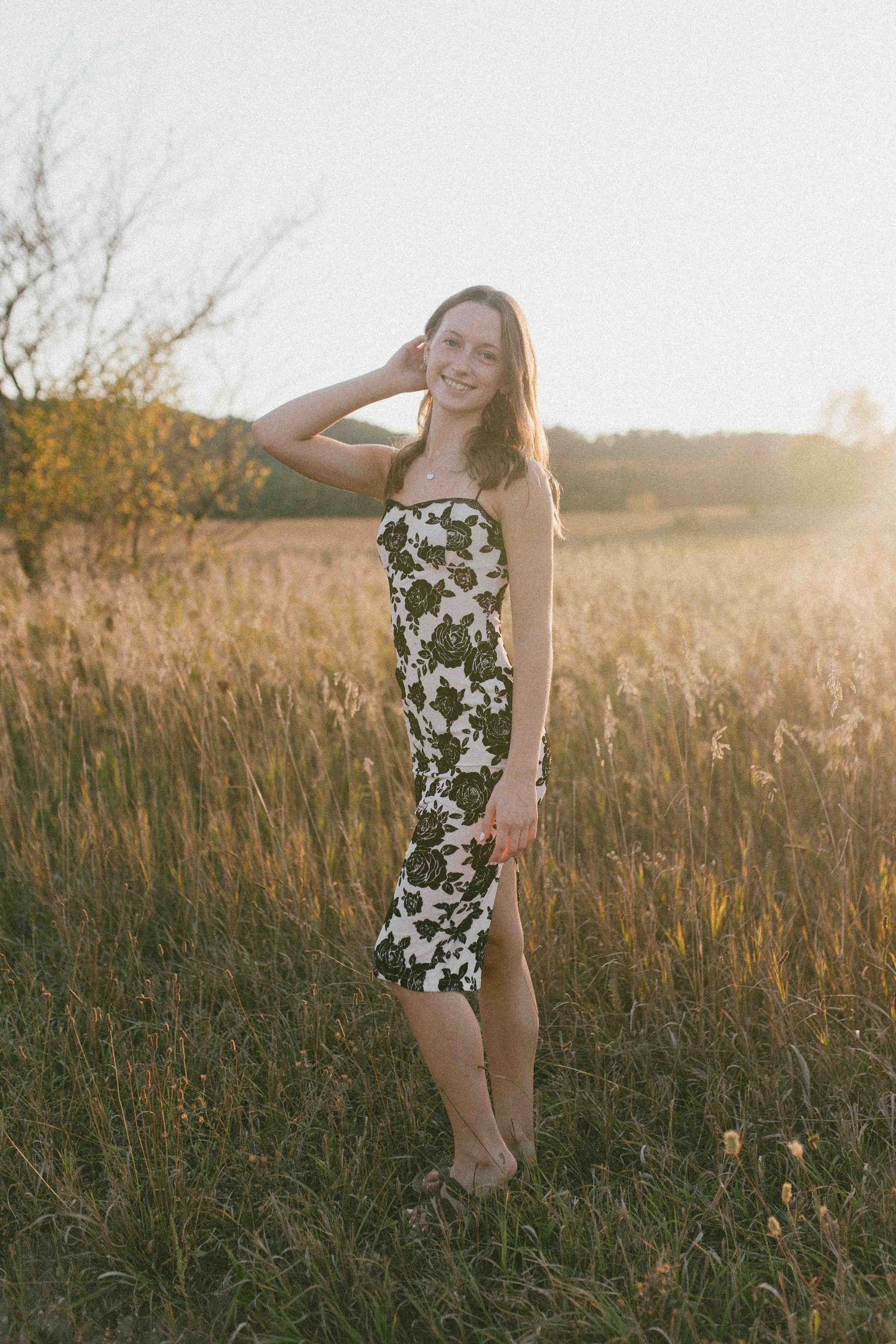 Playful pose in a floral dress among tall grasses during golden hour.