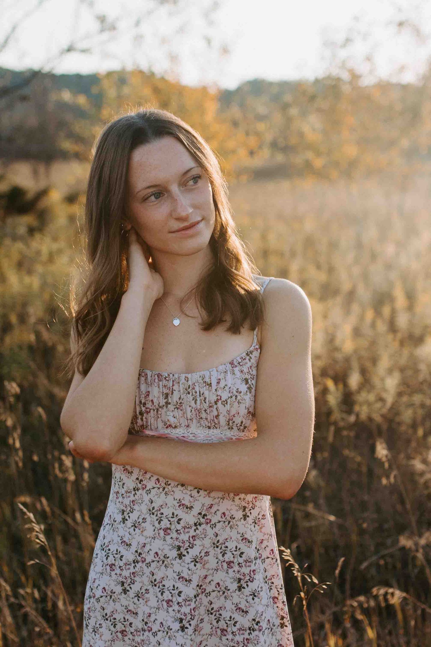 Natural golden hour portrait in a floral dress amidst tall grass and sunset lighting.