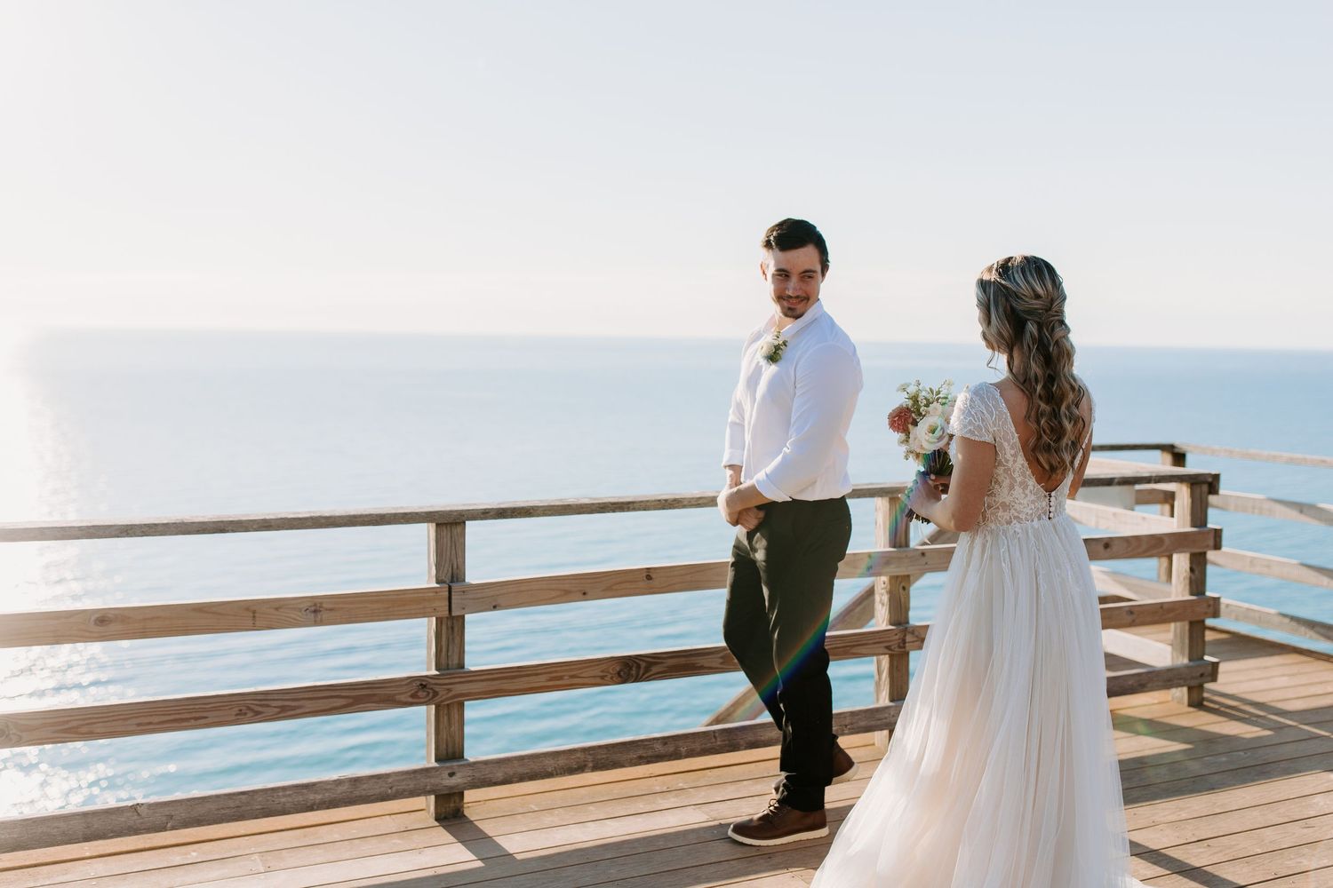 Newlyweds share tender moments on a wooden pier overlooking the ocean.
