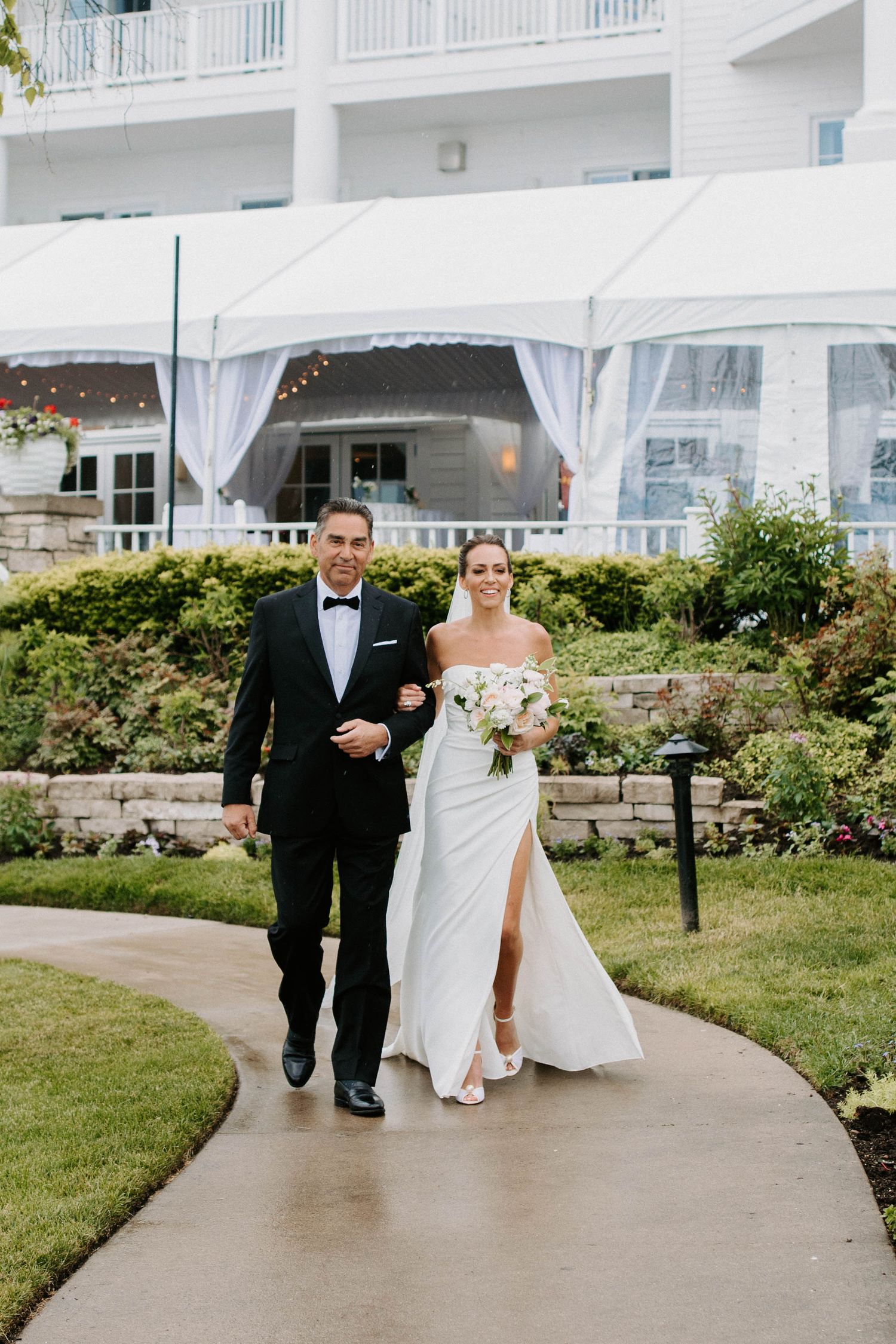 Wedding party members walk along curved pathway with white resort building in background.