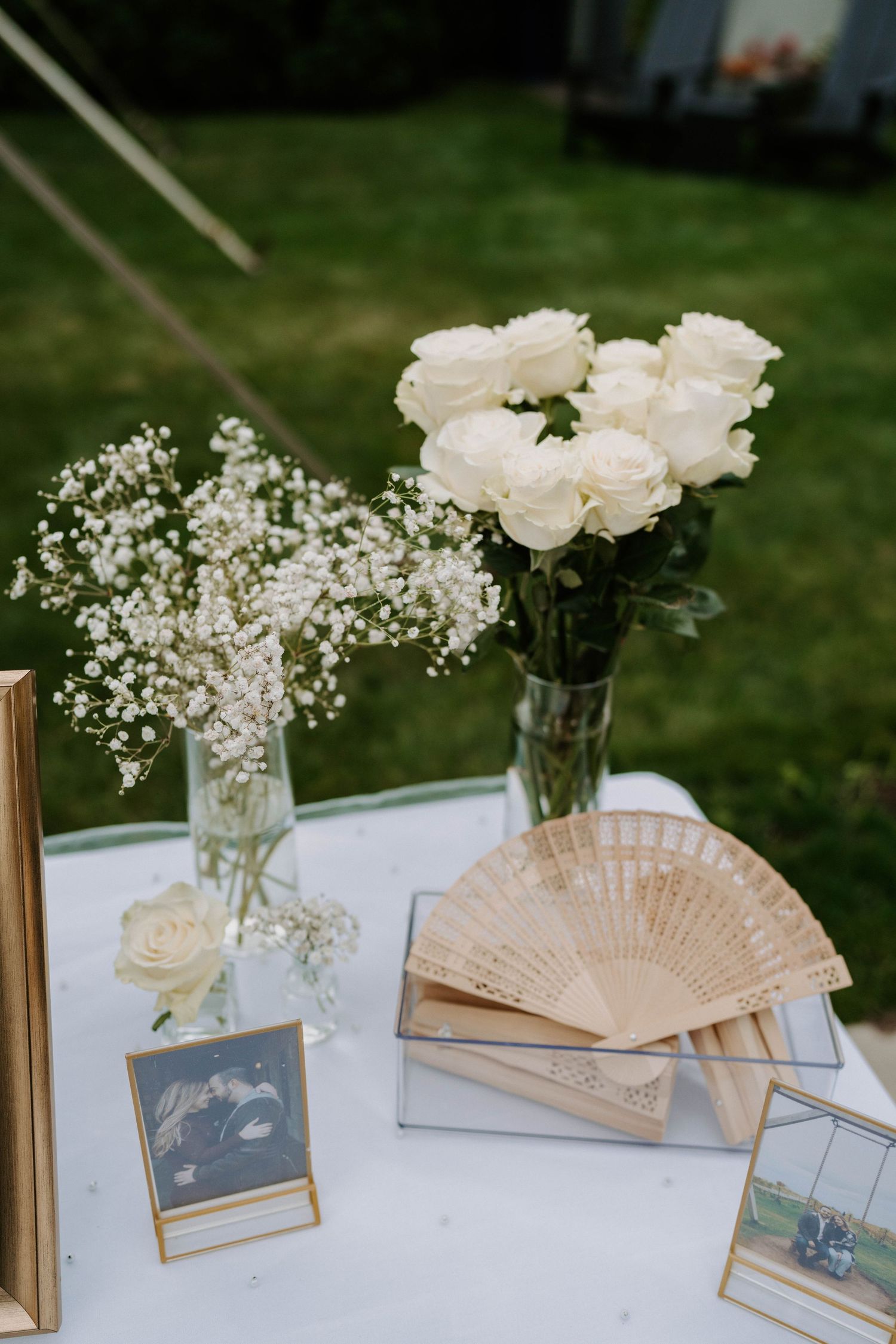 Wedding decor featuring white roses, baby's breath, and decorative fans on display table.