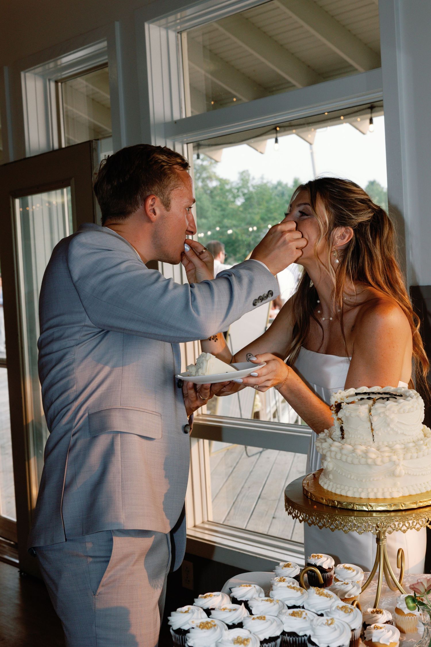 Newlyweds playfully feed each other wedding cake at their reception.