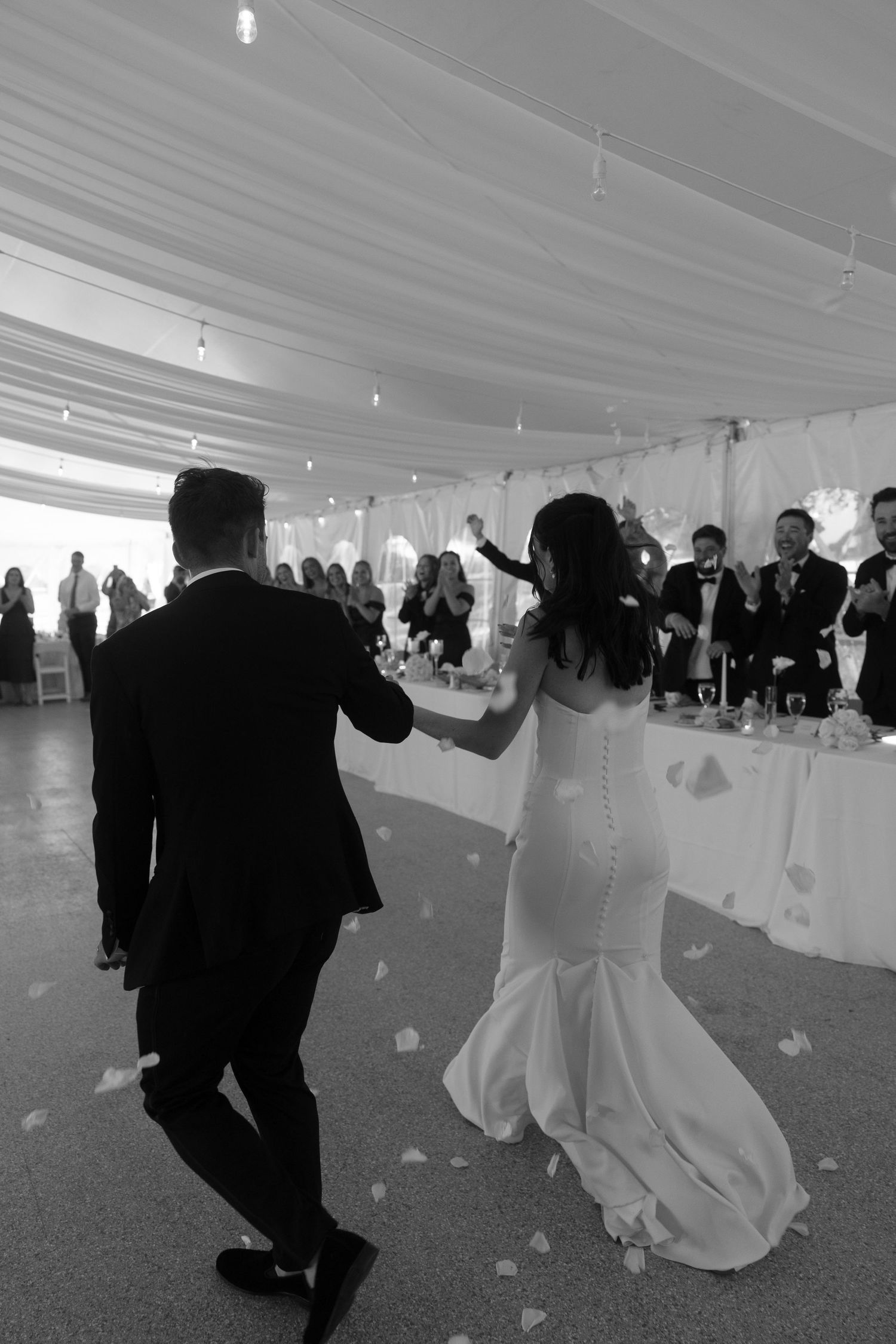 Wedding couple dances together under a white tent while guests throw rose petals during their celebration.