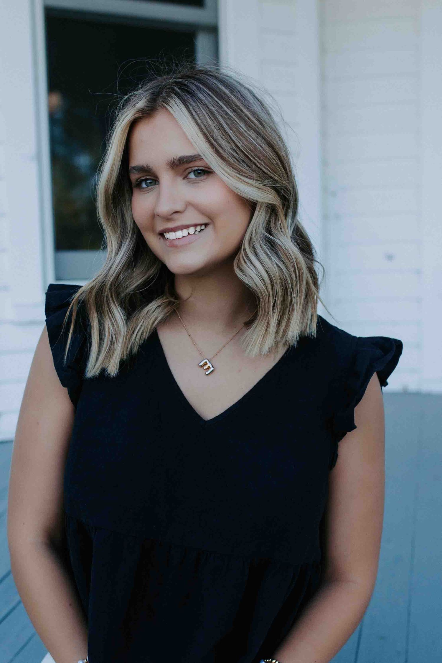 Person wearing black ruffled sleeve top poses on porch.