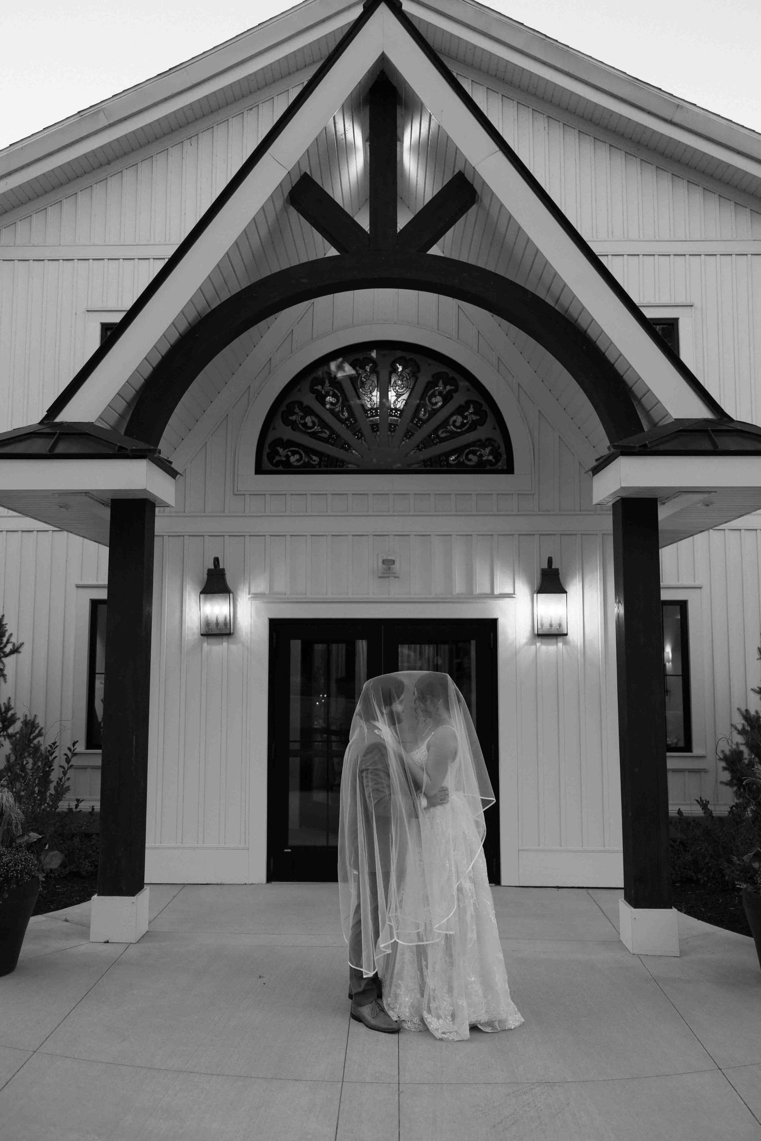 Black and white series showing newlyweds outside a chapel entrance with dramatic lighting.
