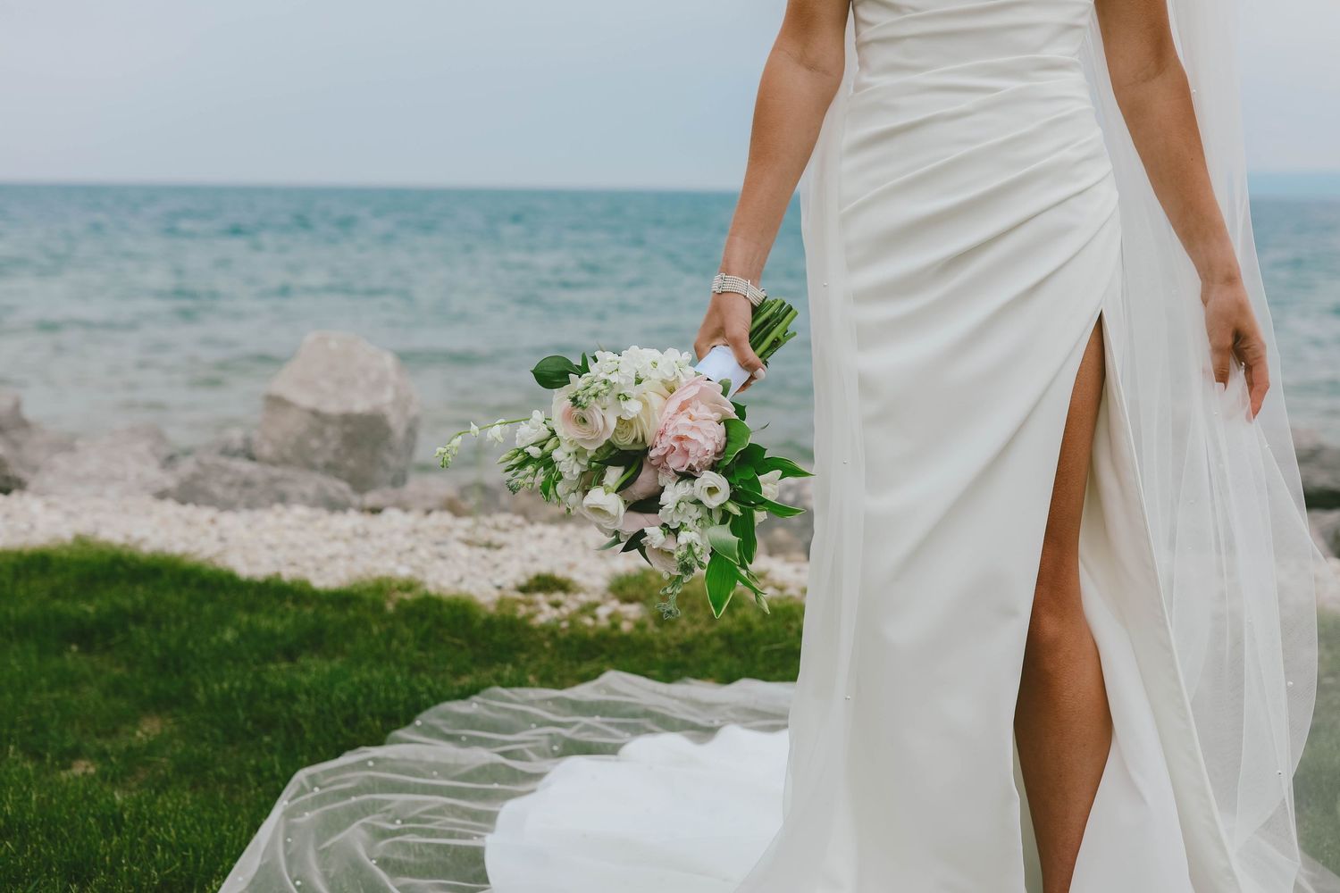Elegant white wedding dress with thigh-high slit photographed against ocean backdrop.