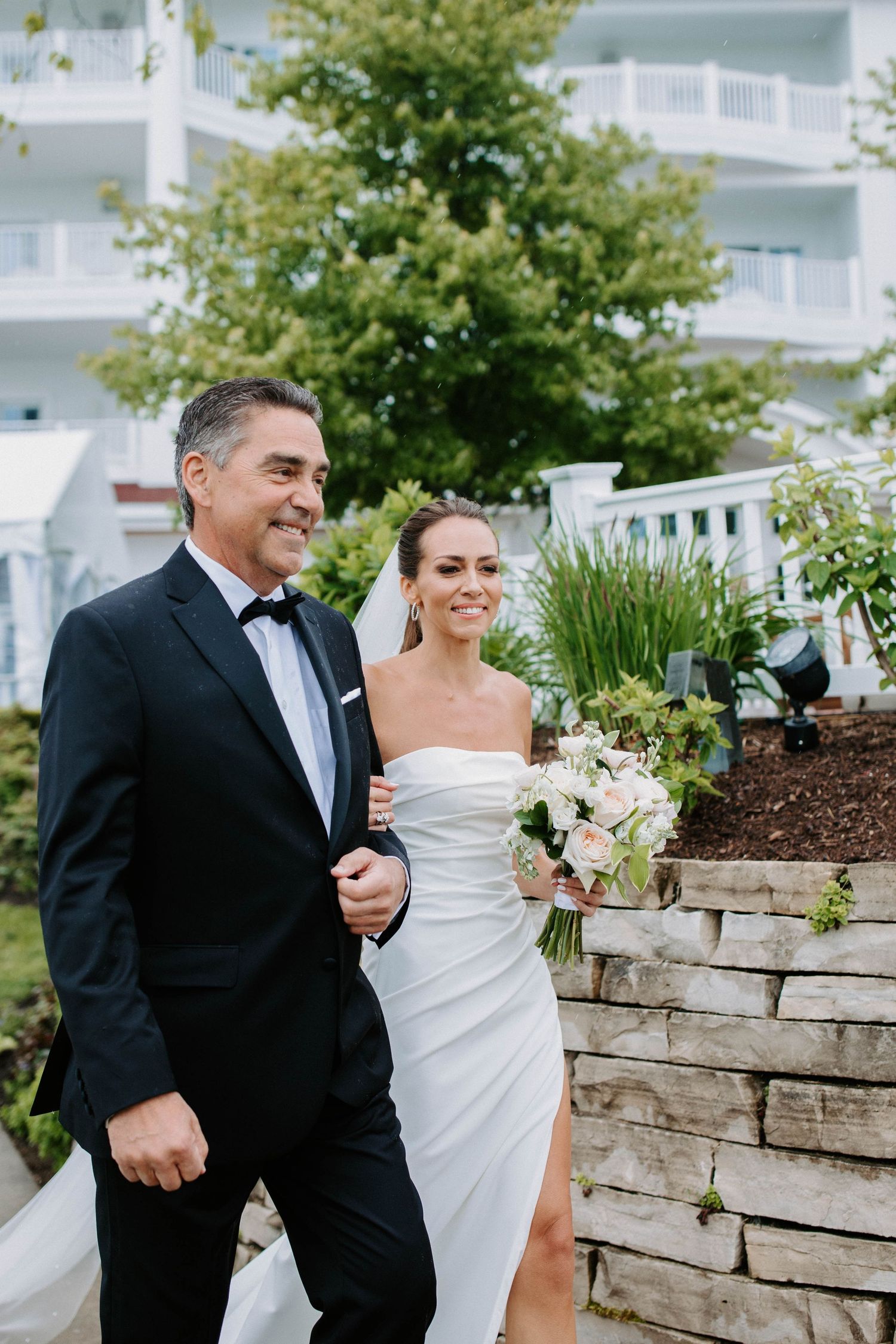 A couple shares a joyful moment together while walking along a stone retaining wall.