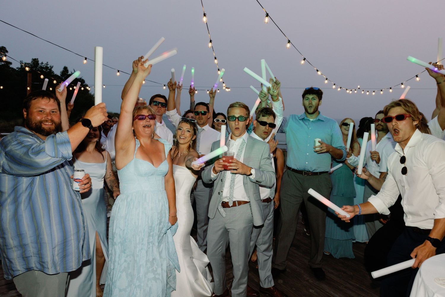 Wedding reception celebration with string lights and guests dancing at dusk.