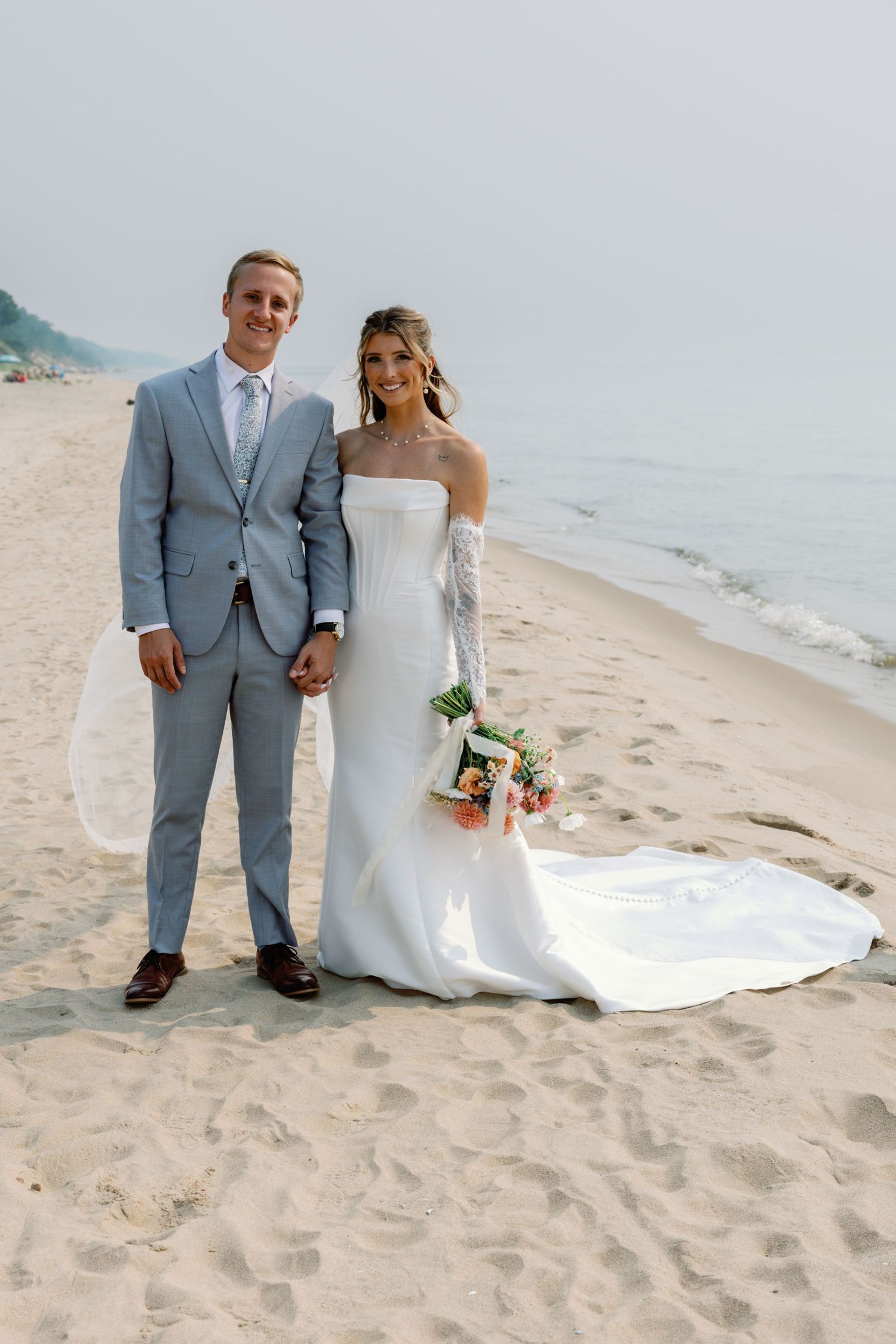 Wedding couple poses for portraits on a sandy beach with ocean waves in background.