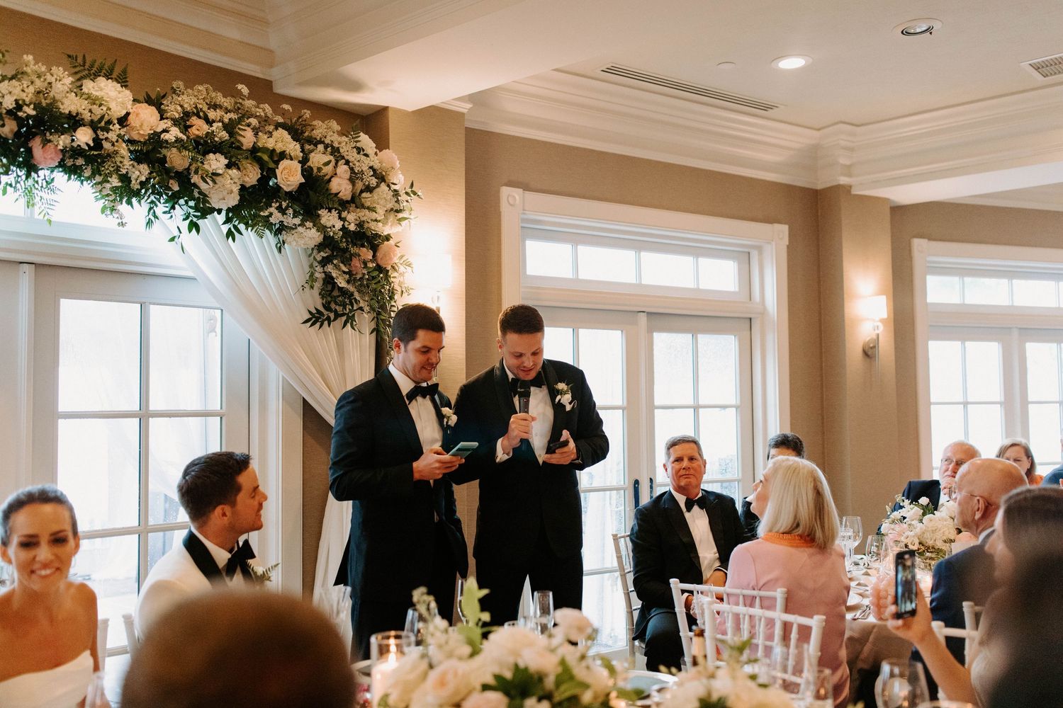 Elegant wedding reception venue with white floral arrangements and natural light streaming through windows.