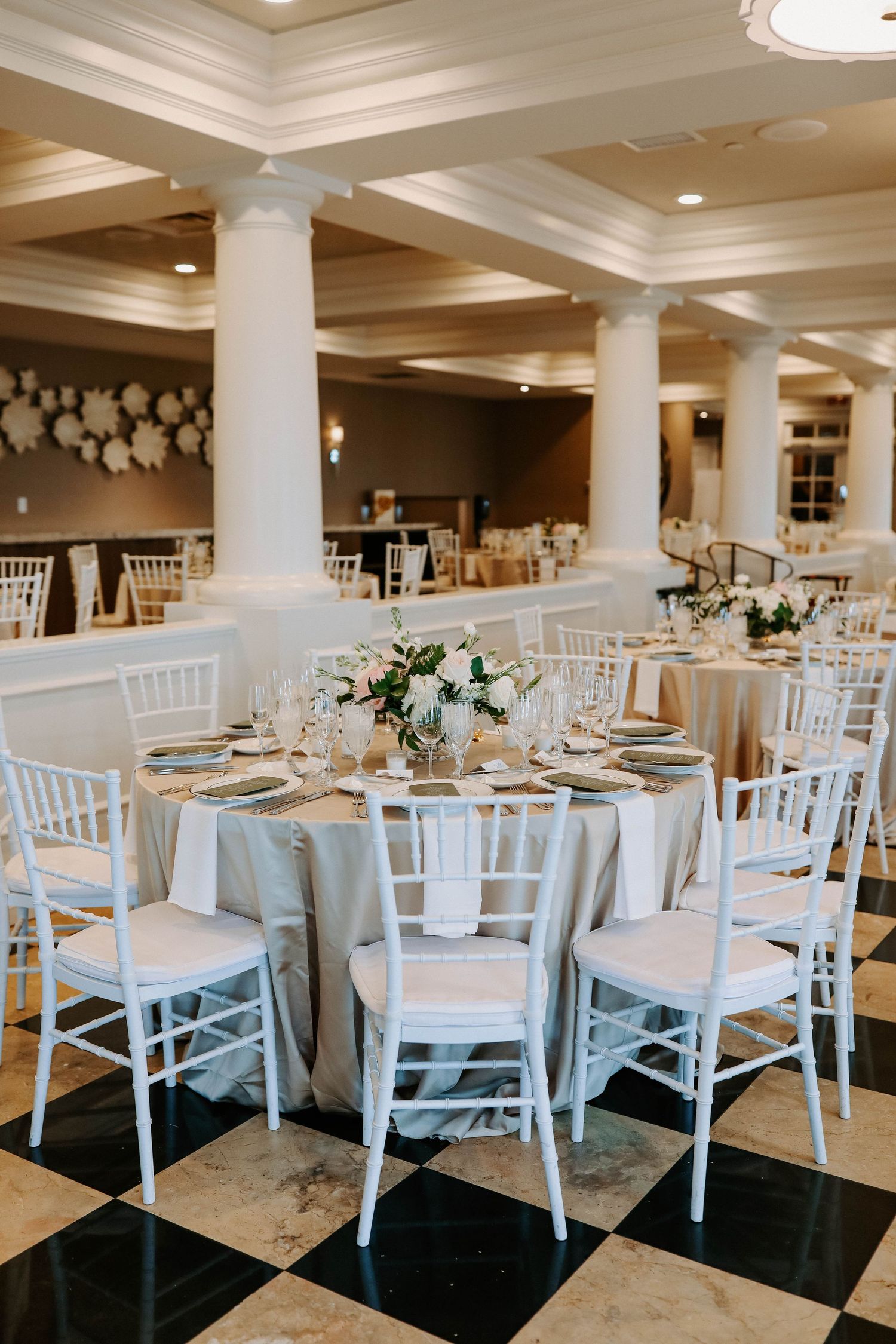 An elegant wedding reception venue with white chiavari chairs and floral centerpieces.