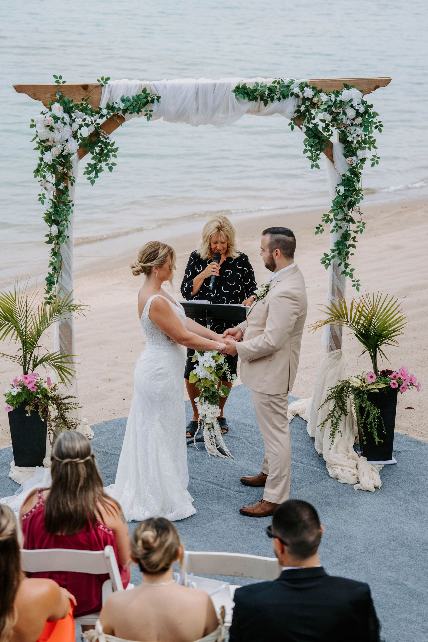 Beachside wedding ceremony with floral arch and palm decorations.