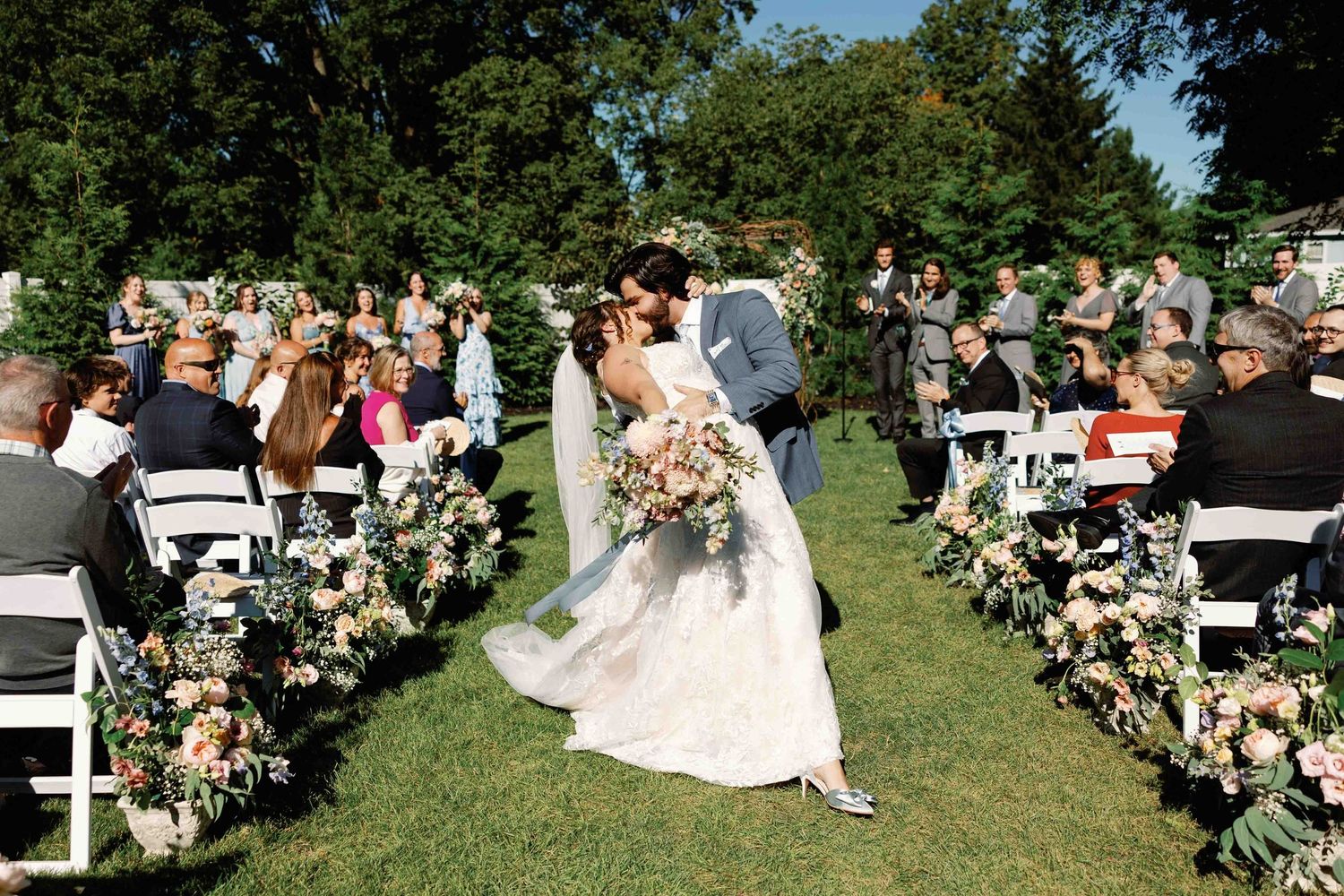 Outdoor wedding ceremony setup with floral arch and white chairs on a sunny summer day.