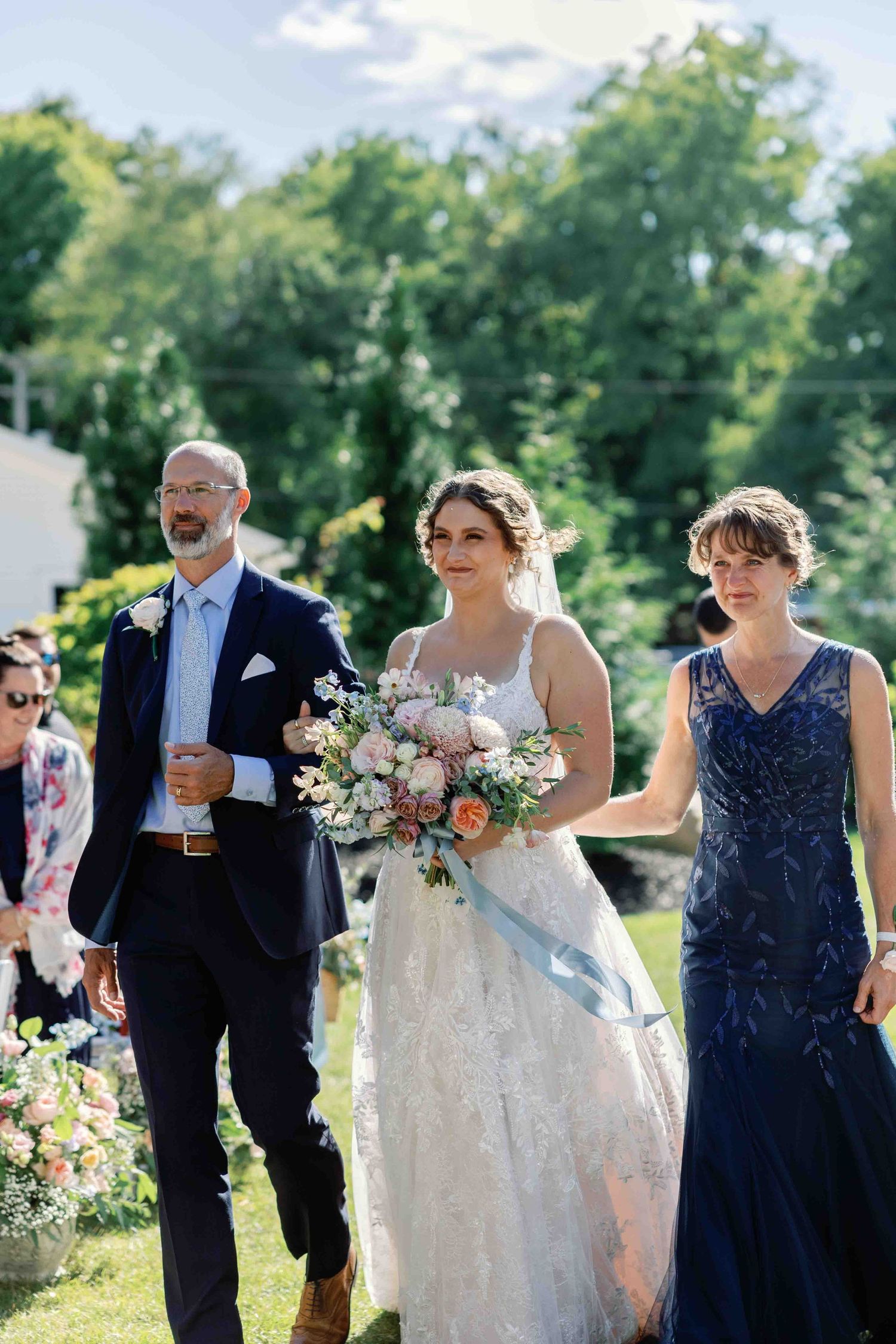 Wedding party walking together outdoors carrying floral bouquets on a sunny day.