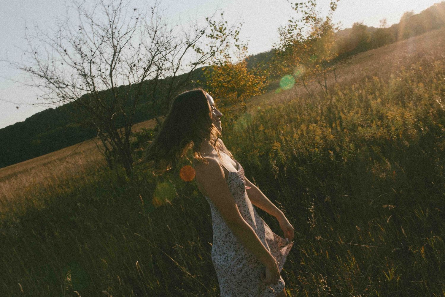 Sun-drenched landscape photo with a figure walking through tall grass at dusk.