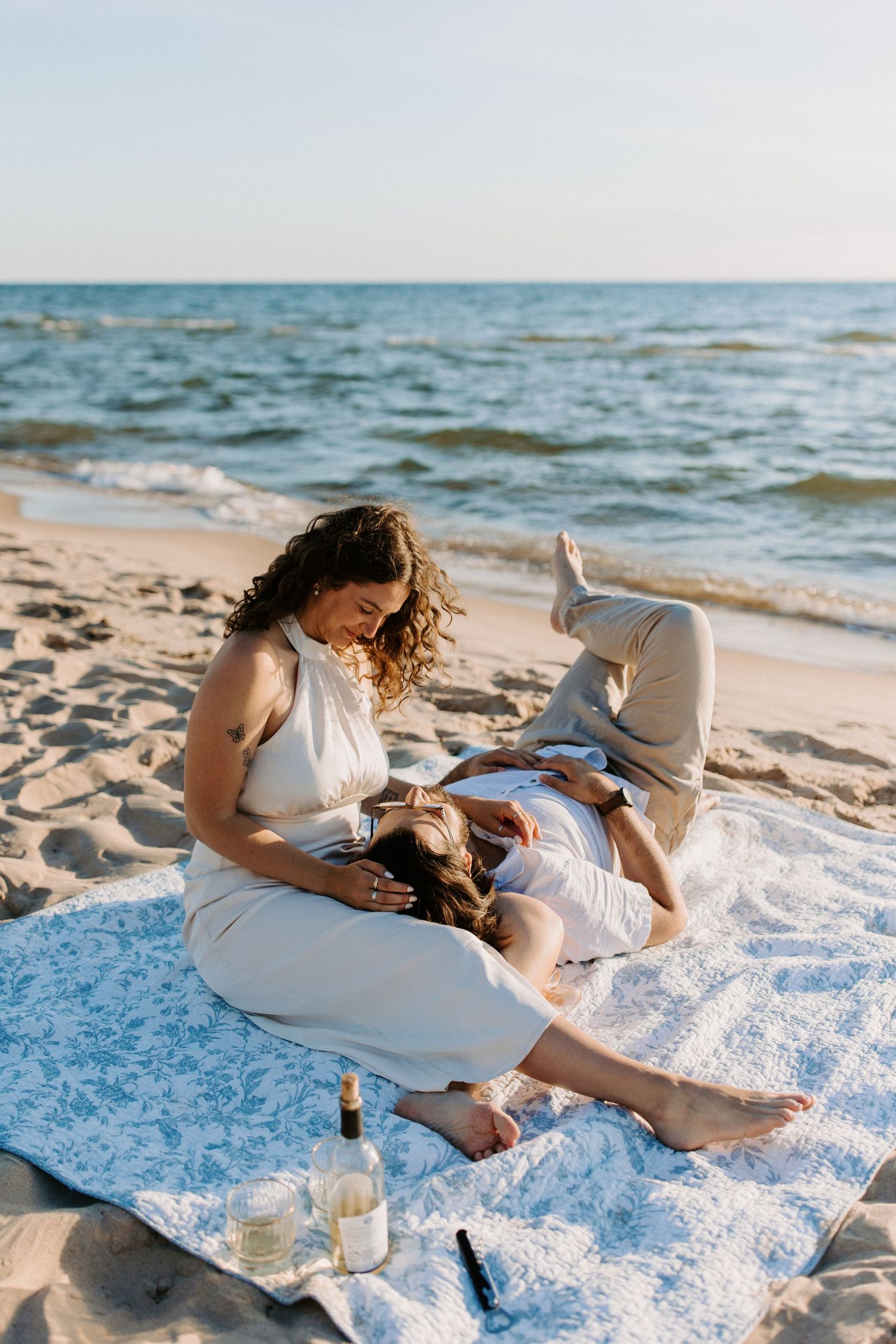 Couple relaxing on a white blanket at the beach during sunset.