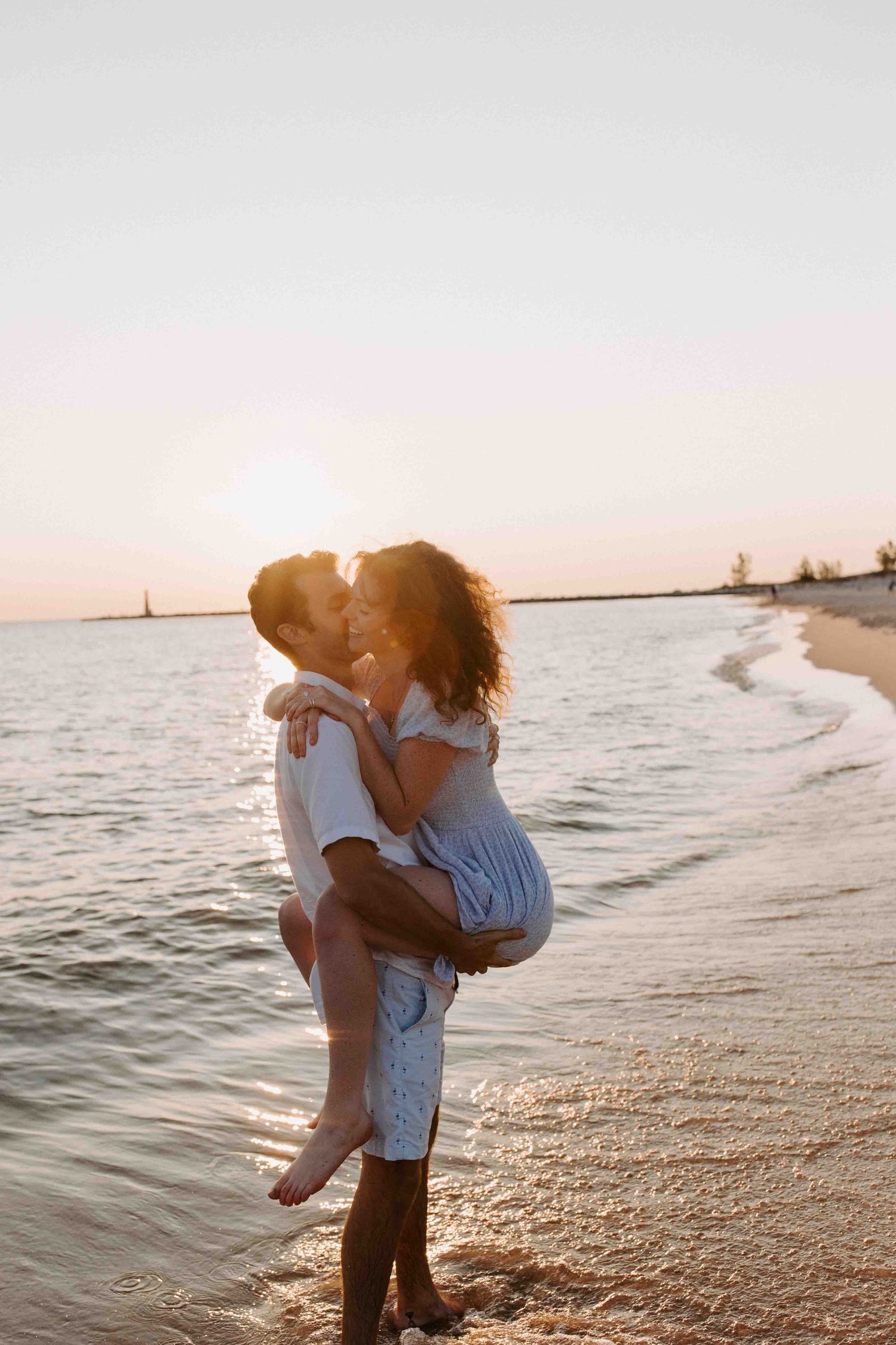 Couple playing and embracing by the ocean during golden hour.