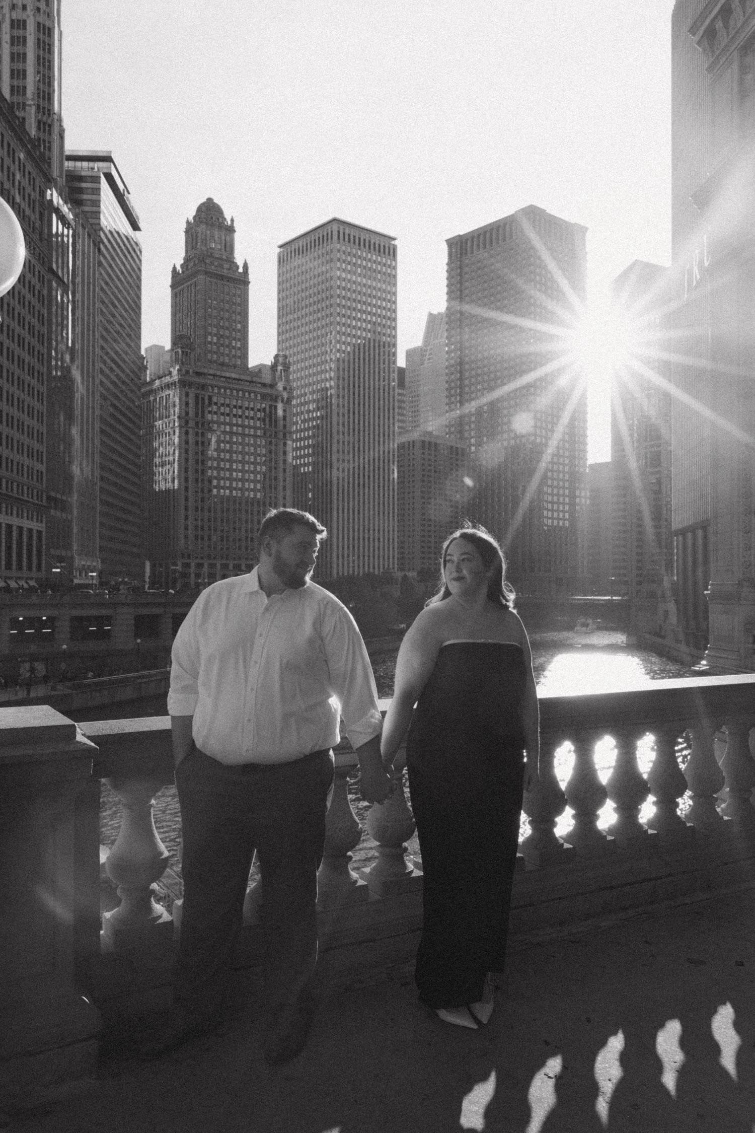A couple shares an intimate moment against a dramatic city skyline with sunburst.