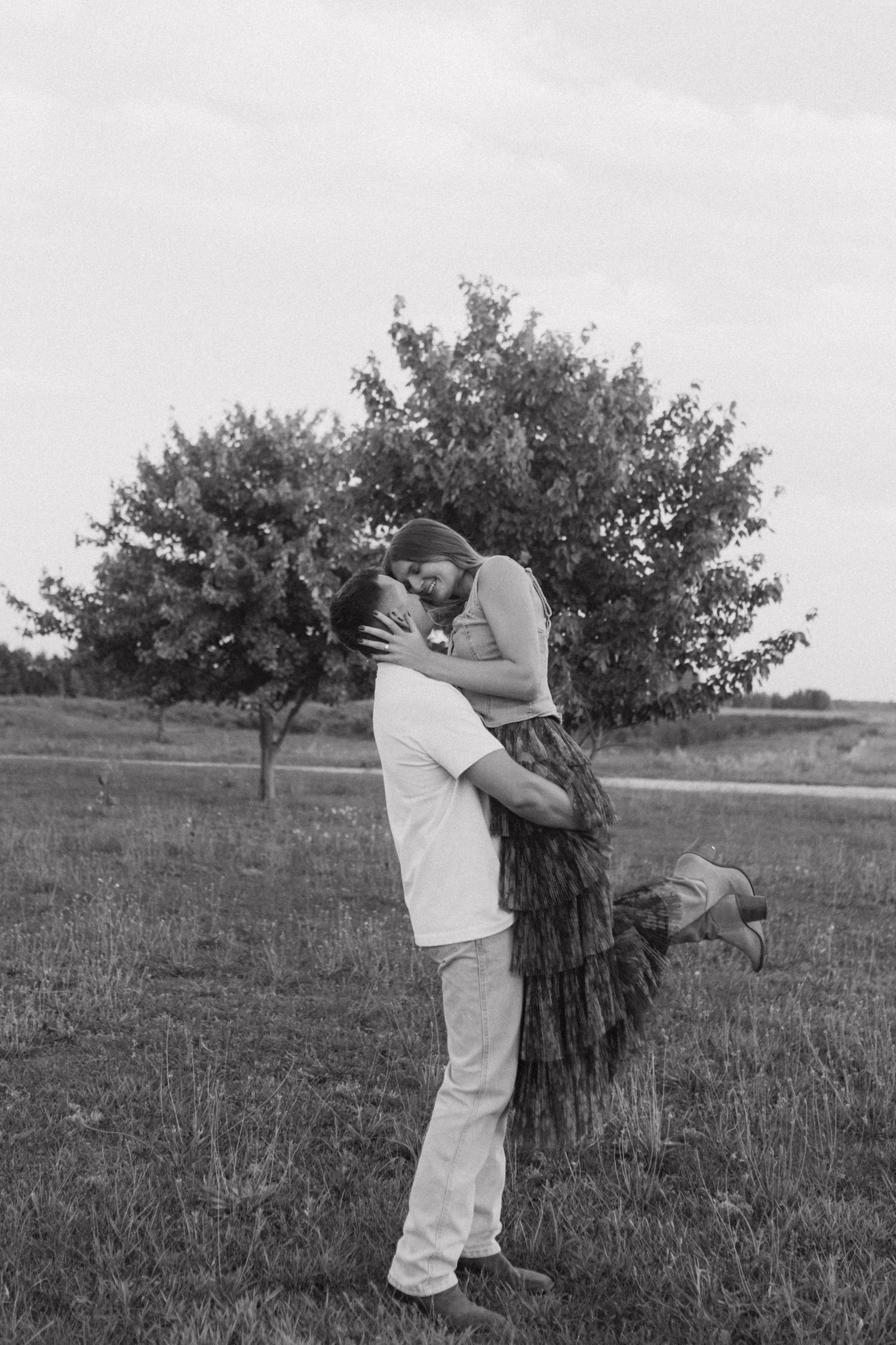 A romantic black and white photo sequence of a couple embracing in a grassy field with trees in the background.