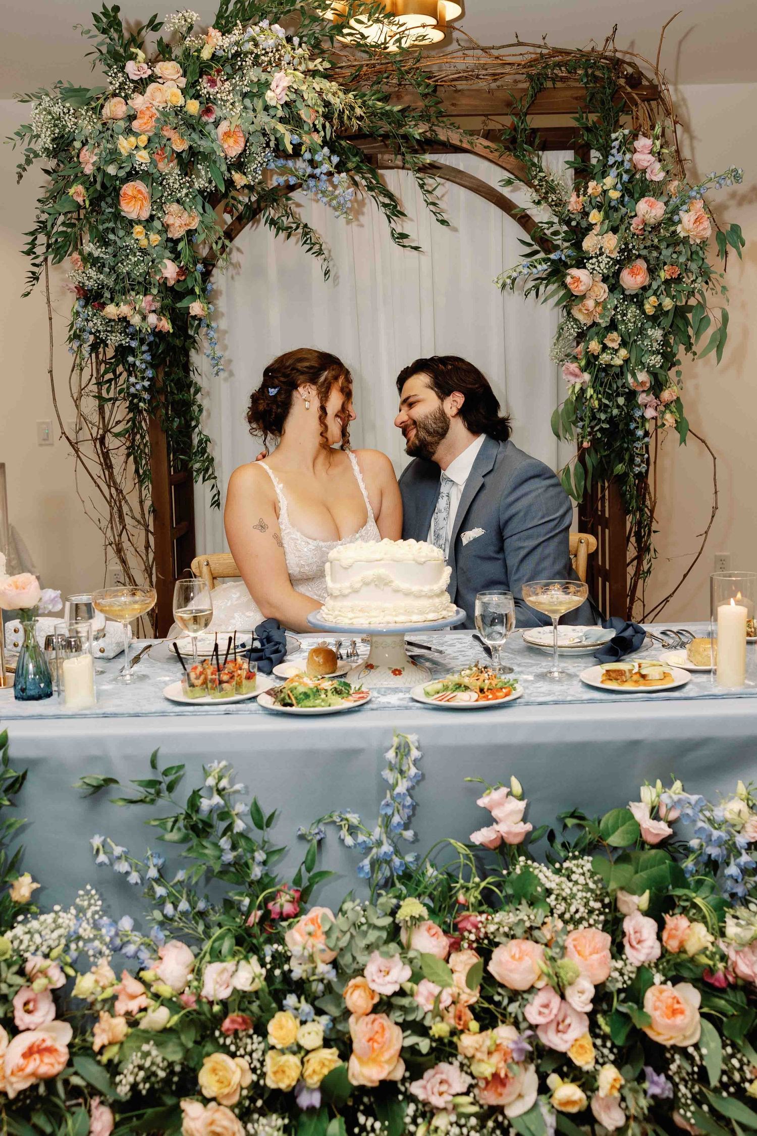 Wedding head table decorated with lush floral arch and romantic pink roses.