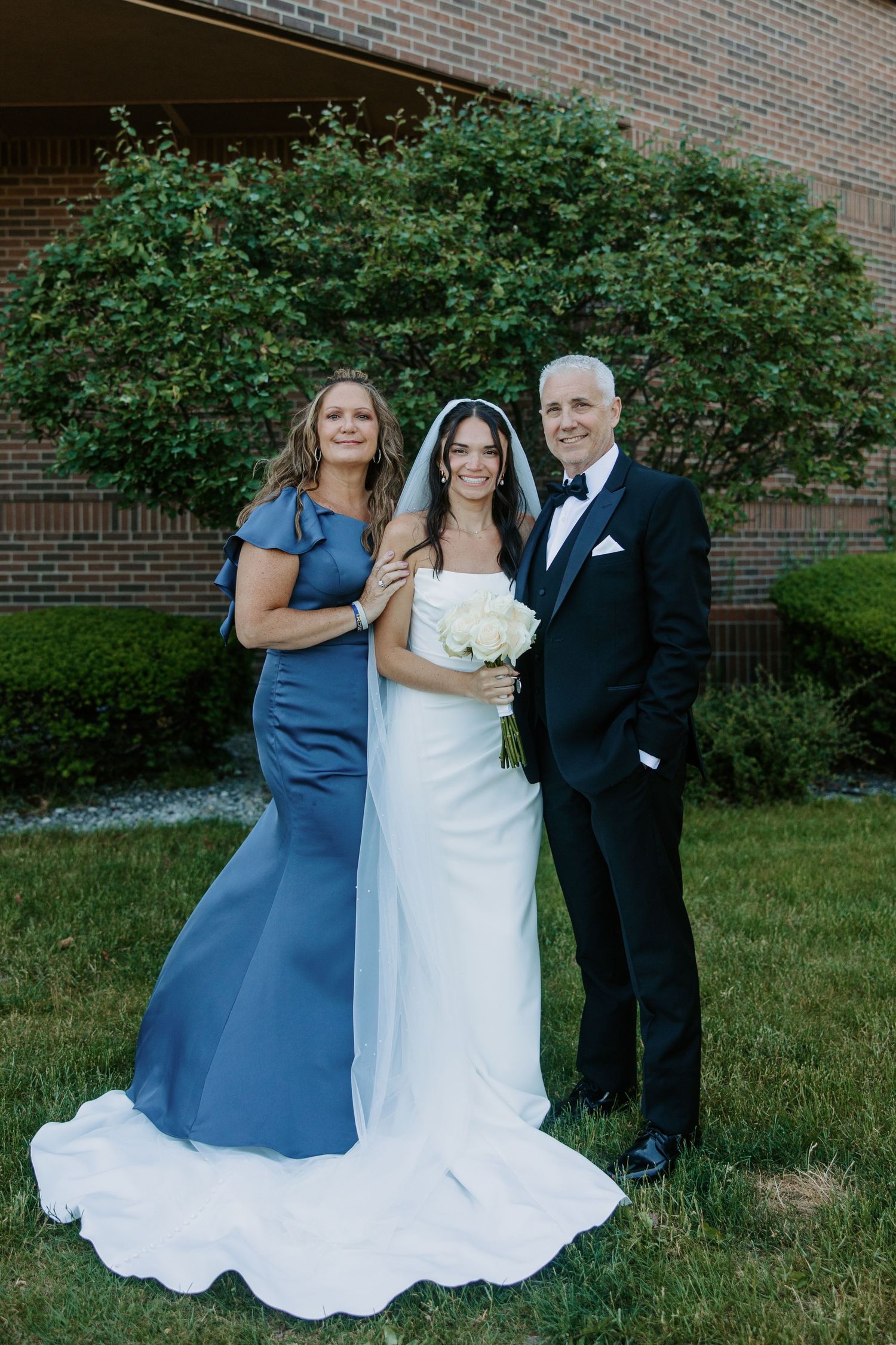 Wedding party poses for formal portraits on grass in front of brick building.