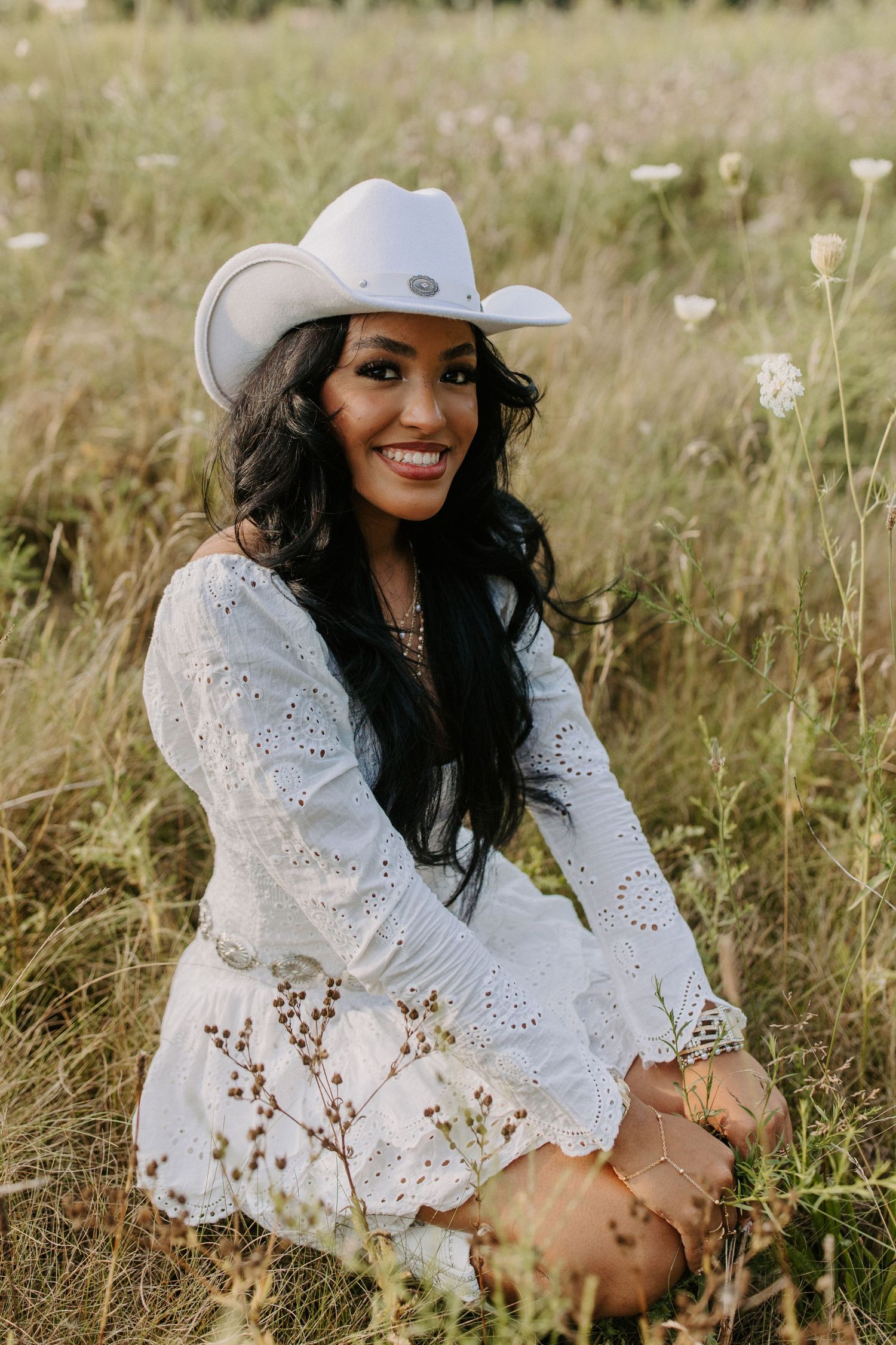 White eyelet dress and sun hat styled in meadow with delicate wildflowers.