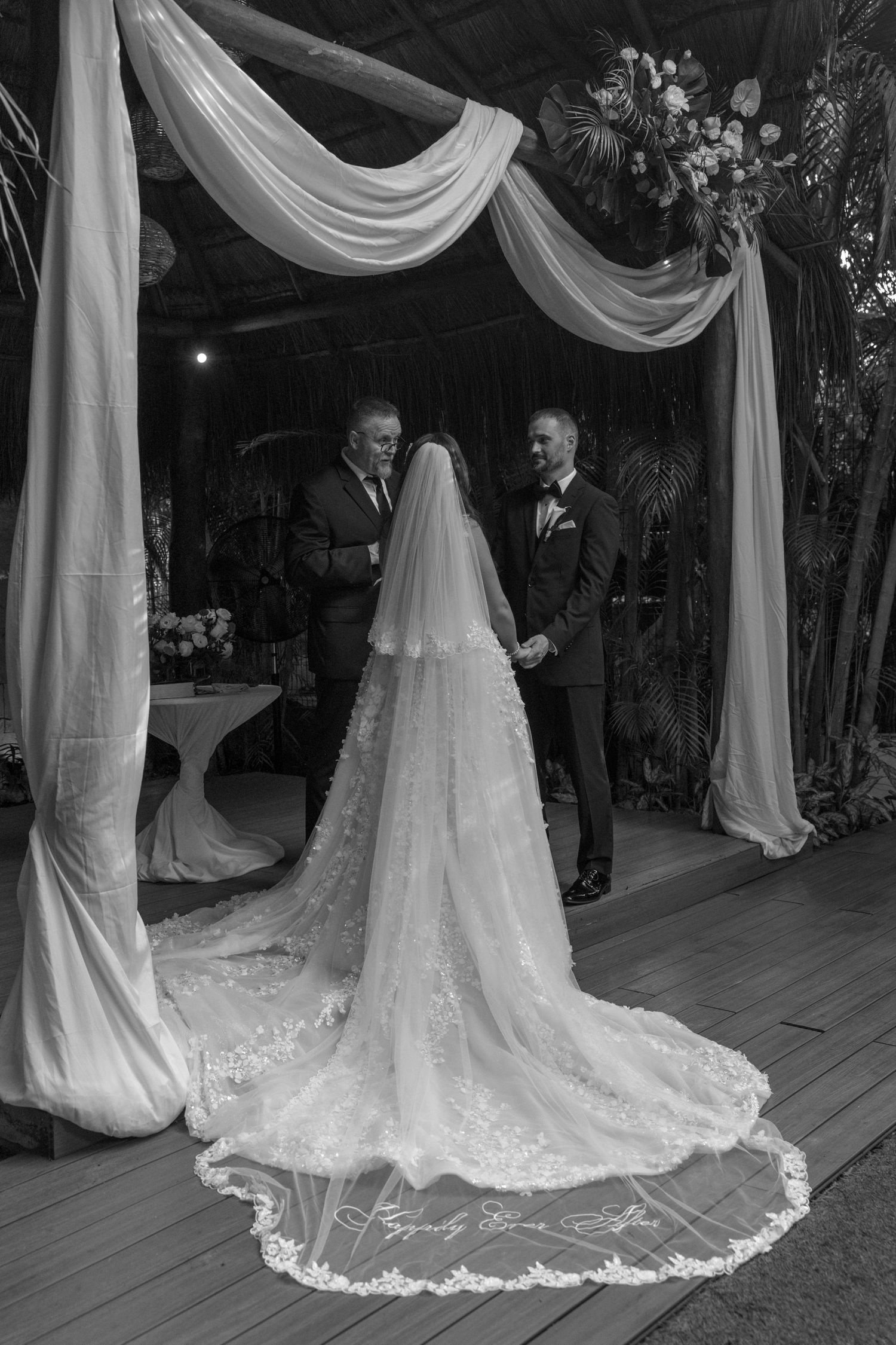 Elegant white wedding dress train displayed on wooden deck with draped fabric decor.