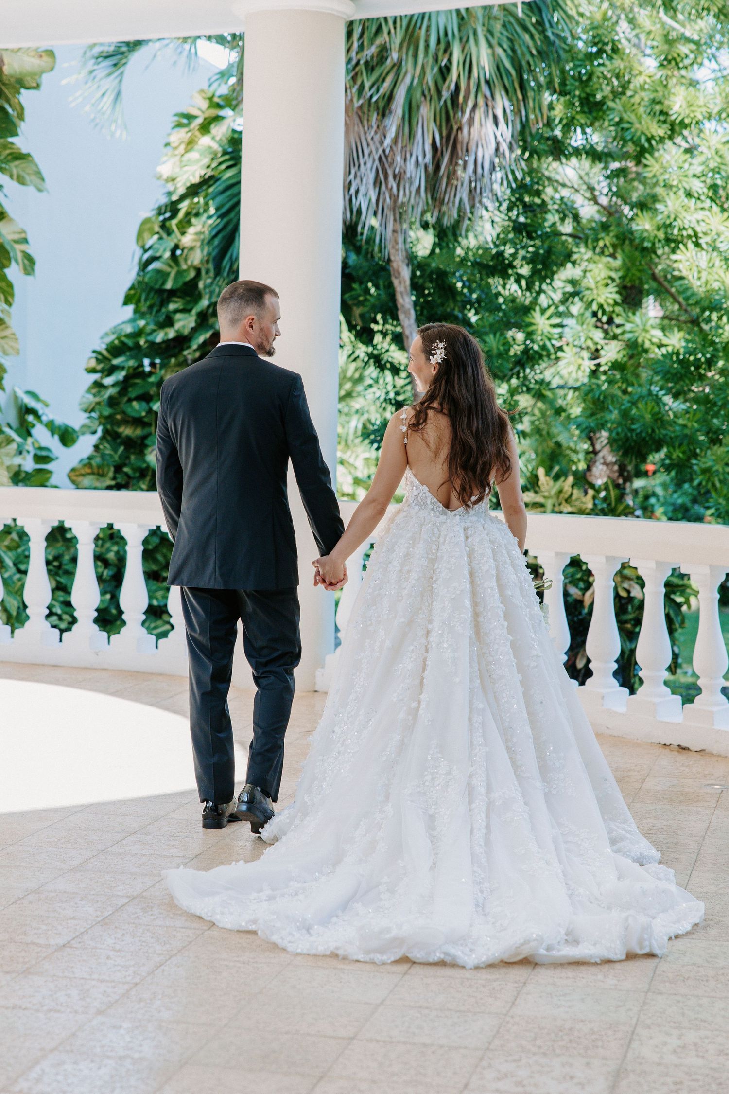Bride in lace wedding gown walks with wedding party along an elegant white balustrade.