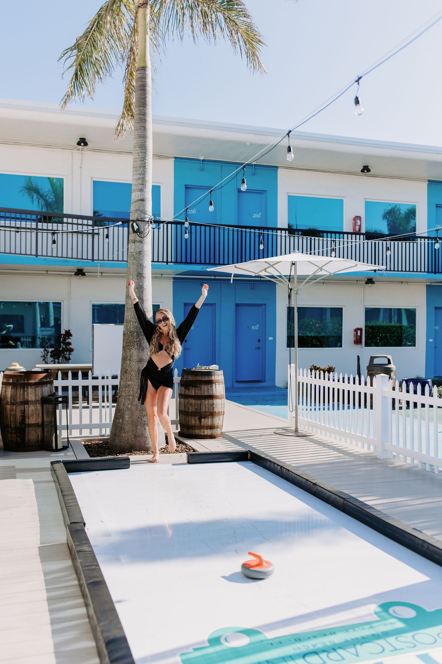 A retro-style motel with turquoise accents features a poolside scene with string lights and palm trees.