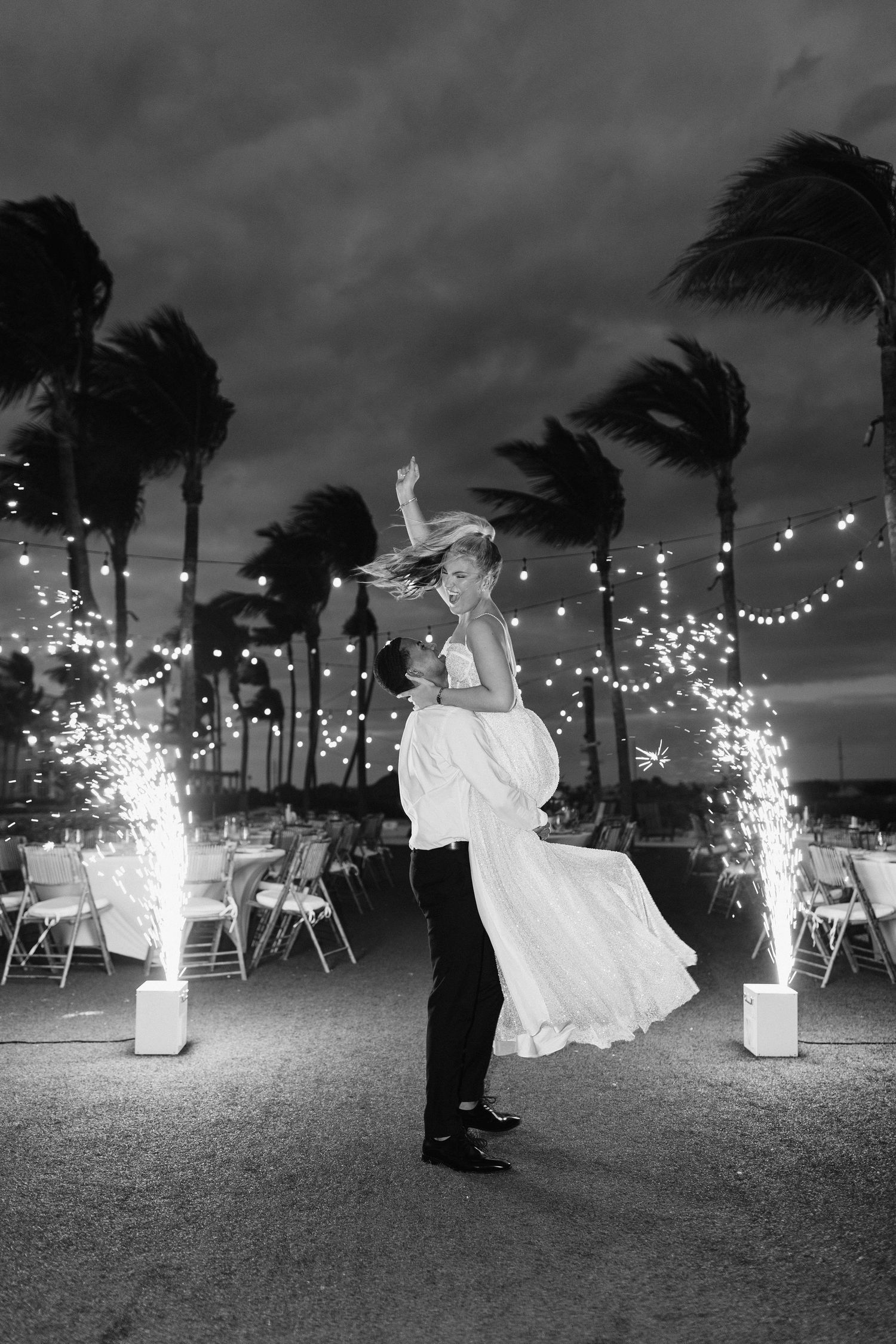 Wedding celebration at night with sparklers and dancing silhouettes against string lights.