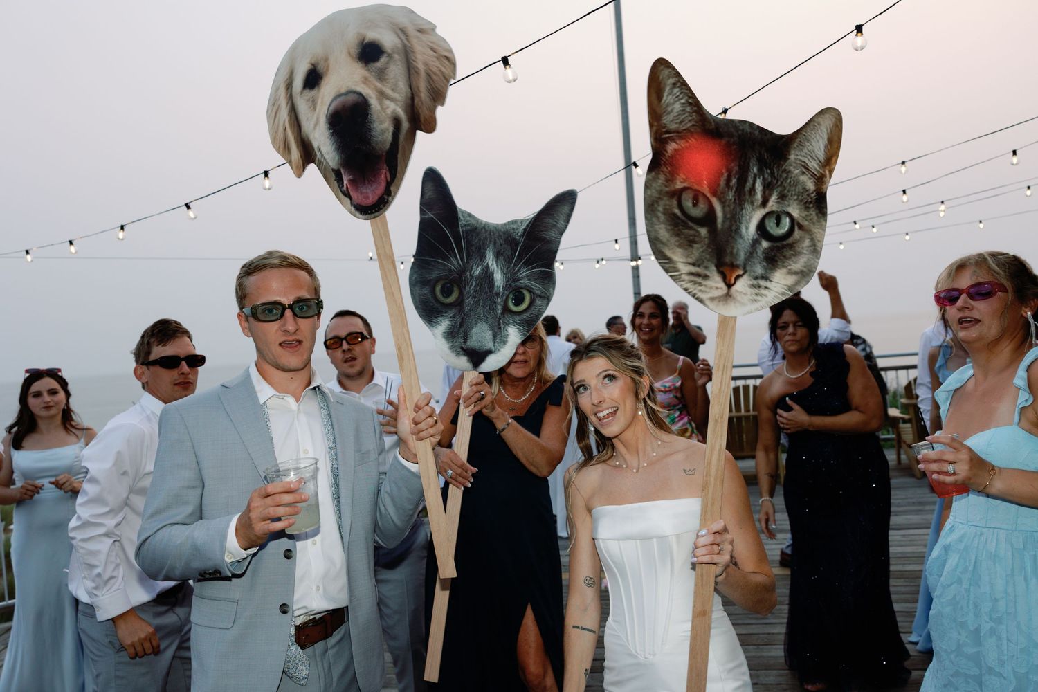 Wedding reception guests celebrating with pets under string lights at dusk.