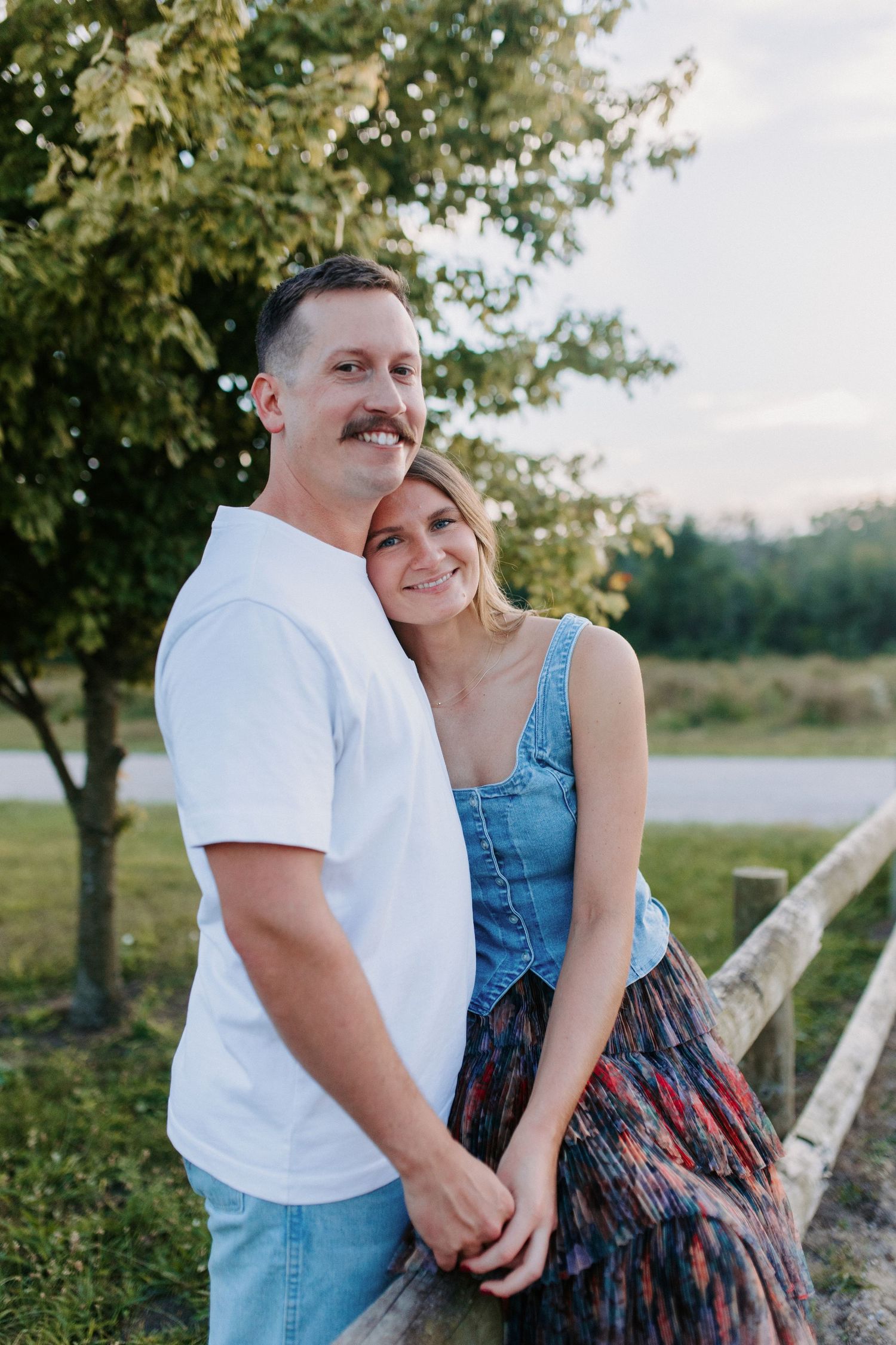 A couple sitting together on a wooden fence during an outdoor photoshoot.