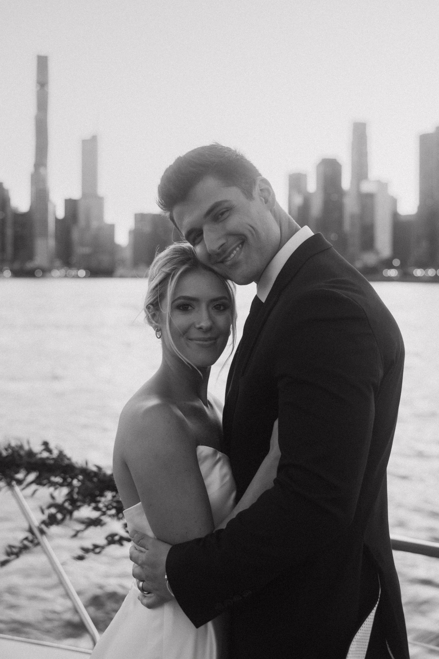 Black and white wedding portraits on boat with city skyline backdrop.