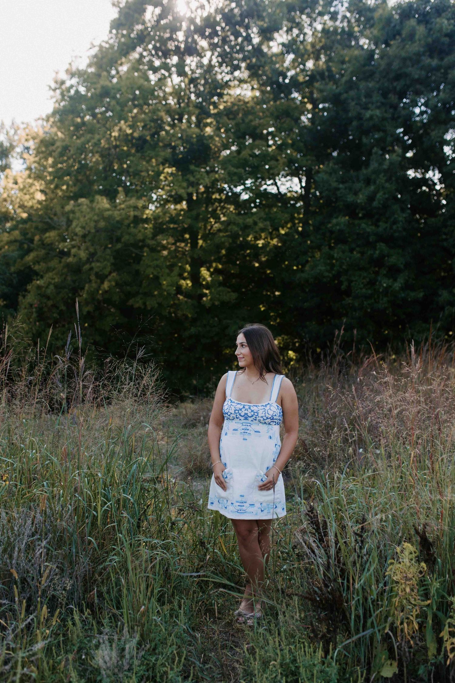 Lifestyle portrait in a white and blue patterned dress among tall grass.