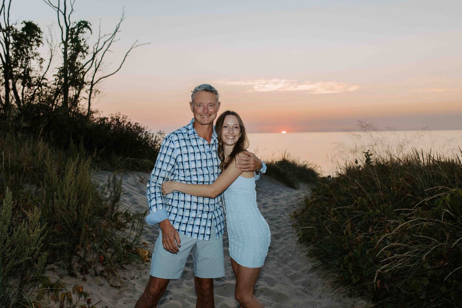 People dancing and having fun on a sandy beach path with the ocean visible at sunset.