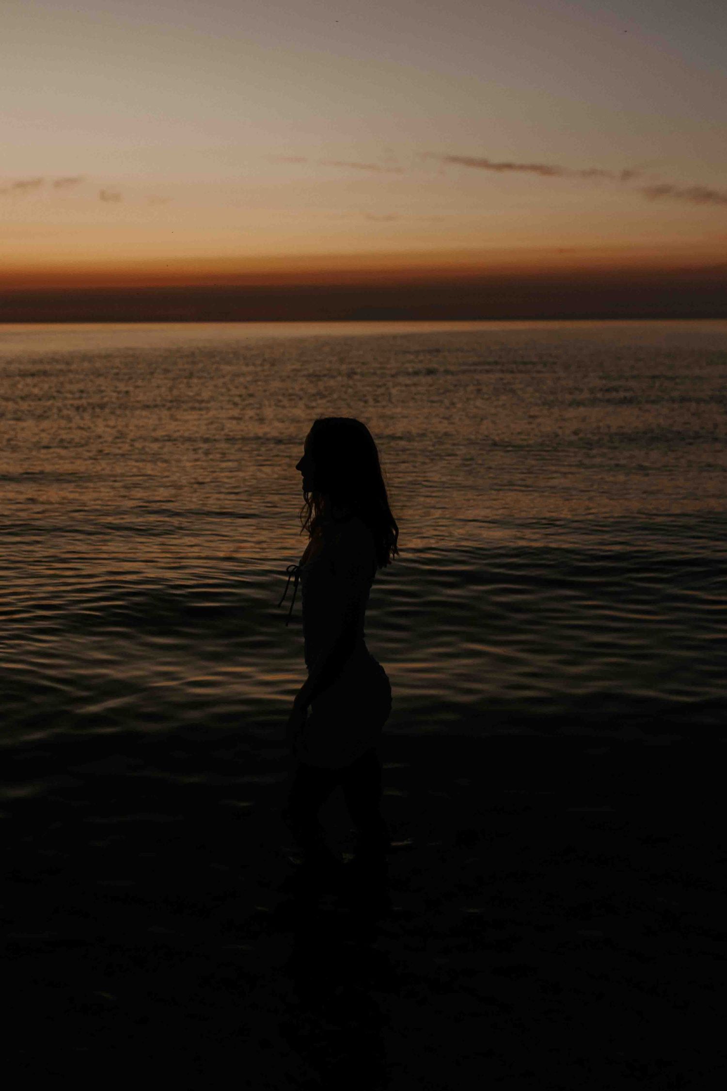 Silhouettes against a dramatic orange sunset over calm ocean waters.