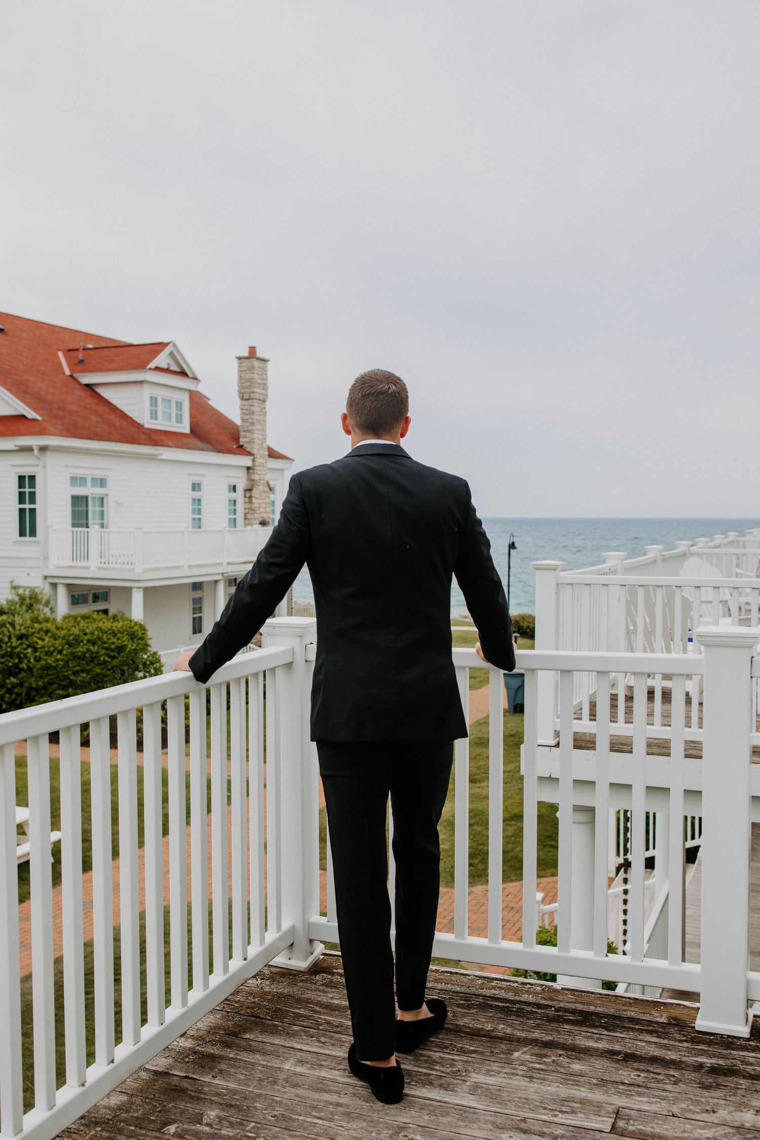 Wedding party member in formal attire walking along white coastal railing.