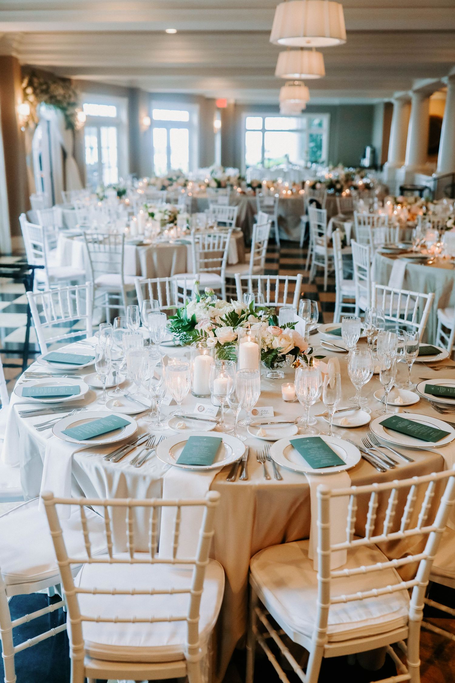 Elegant wedding reception room with white chiavari chairs and round tables set for dining.