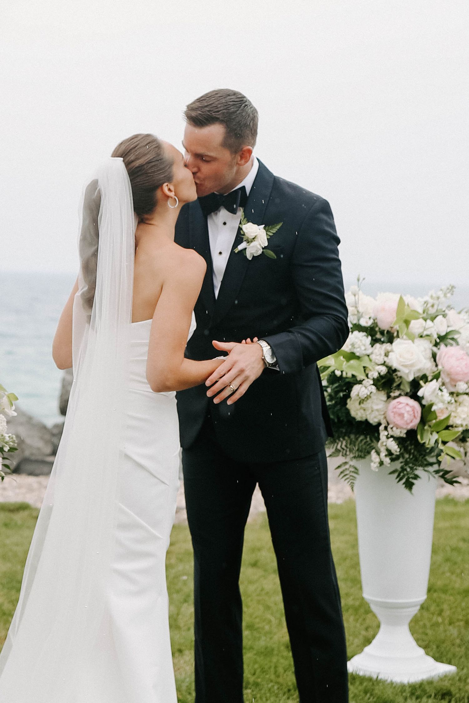 Romantic wedding moment captured outdoors with white floral arrangements in the background.