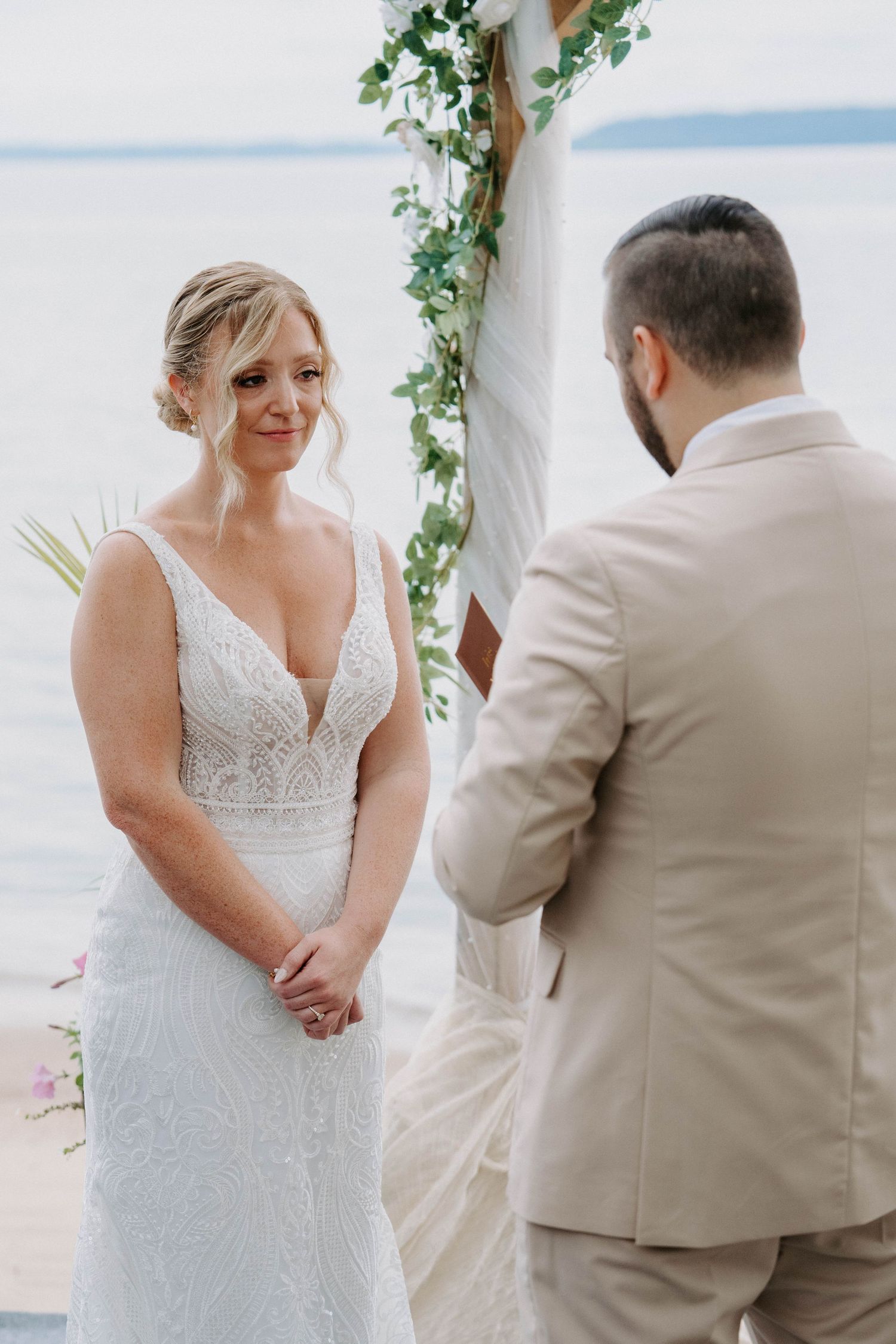 A romantic beach wedding ceremony with a white-draped arch adorned with greenery and ocean views in the background.