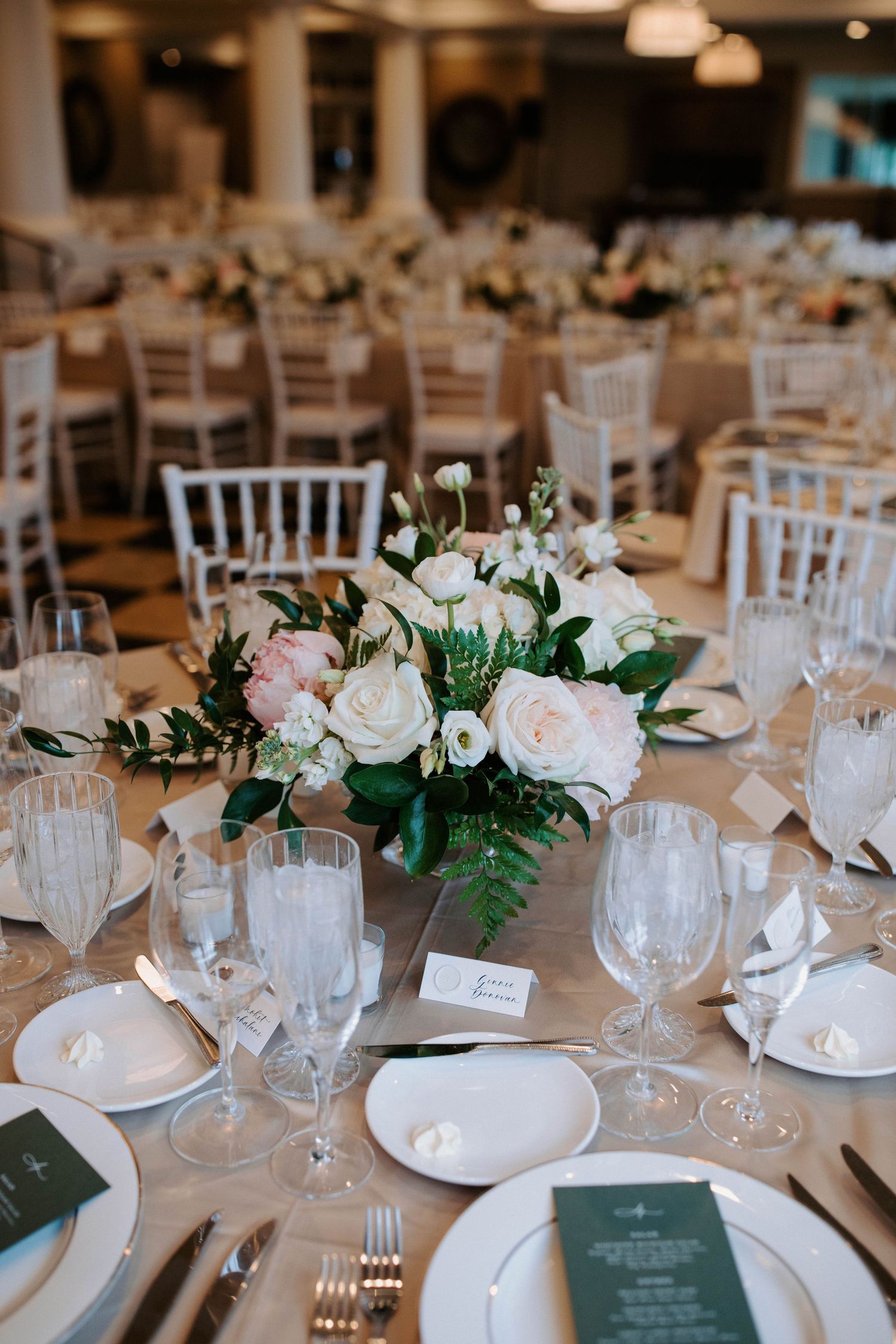 A wedding reception table with pink and white floral centerpiece and formal place settings.