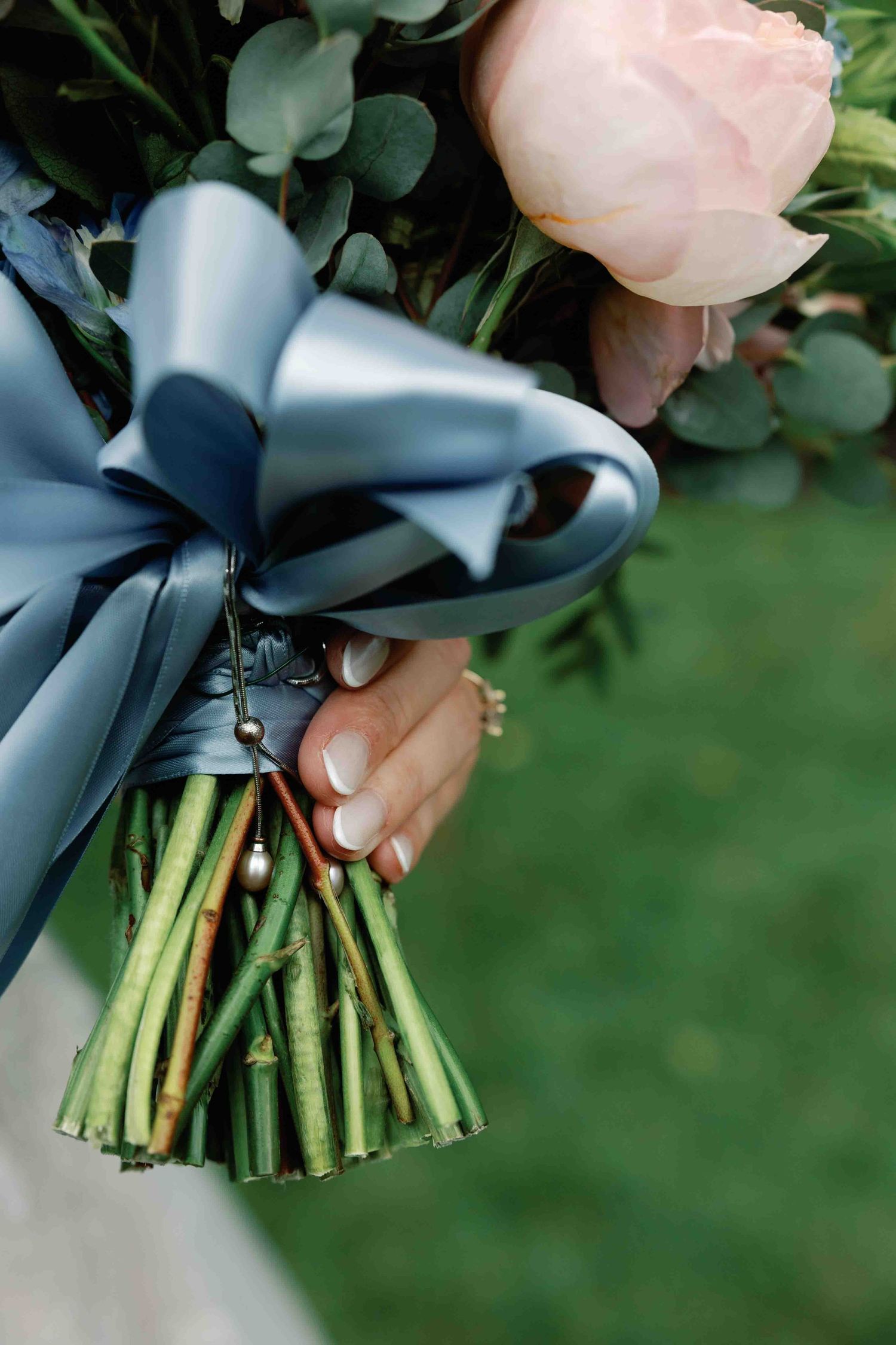 Close-up of a bridal bouquet wrapped with a blue silk ribbon against a green background.