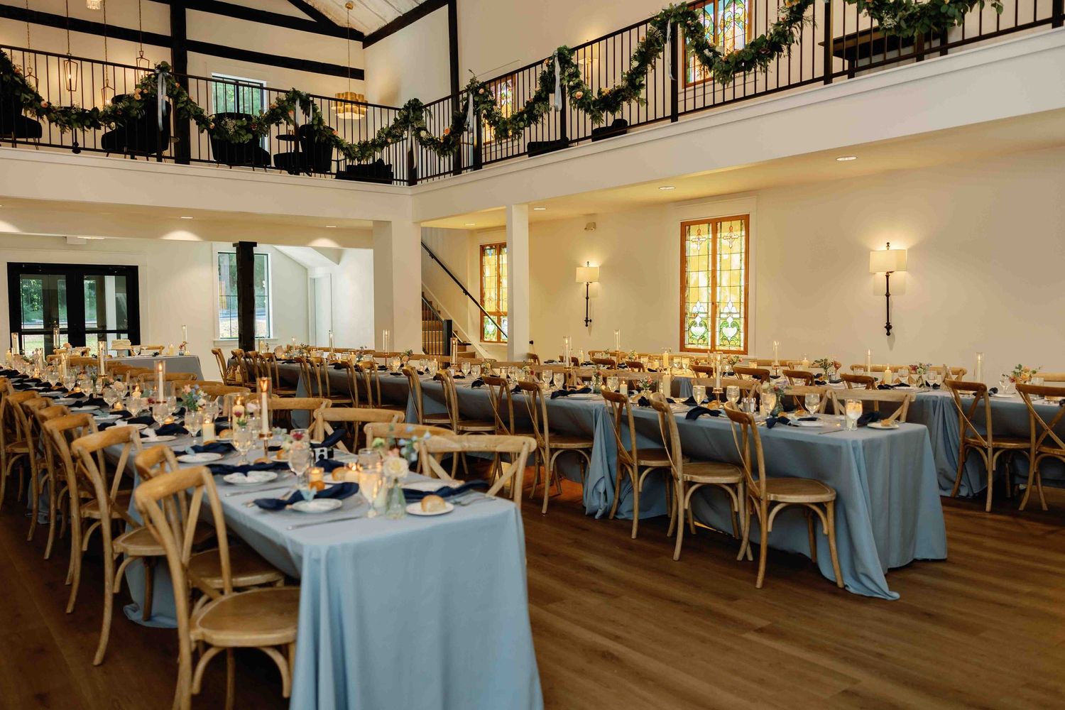 Reception hall decorated with elegant garlands and set with light blue tablecloths and cross-back chairs.