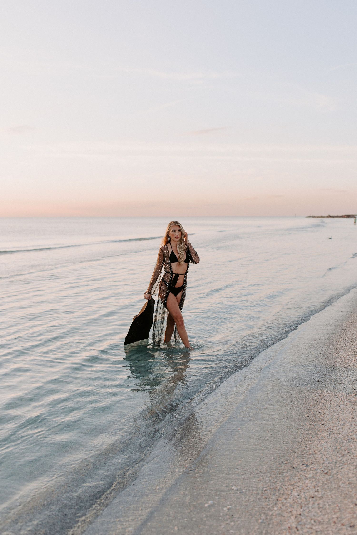 A beachside scene at sunset with gentle waves lapping at the shore and a paddleboard in view.