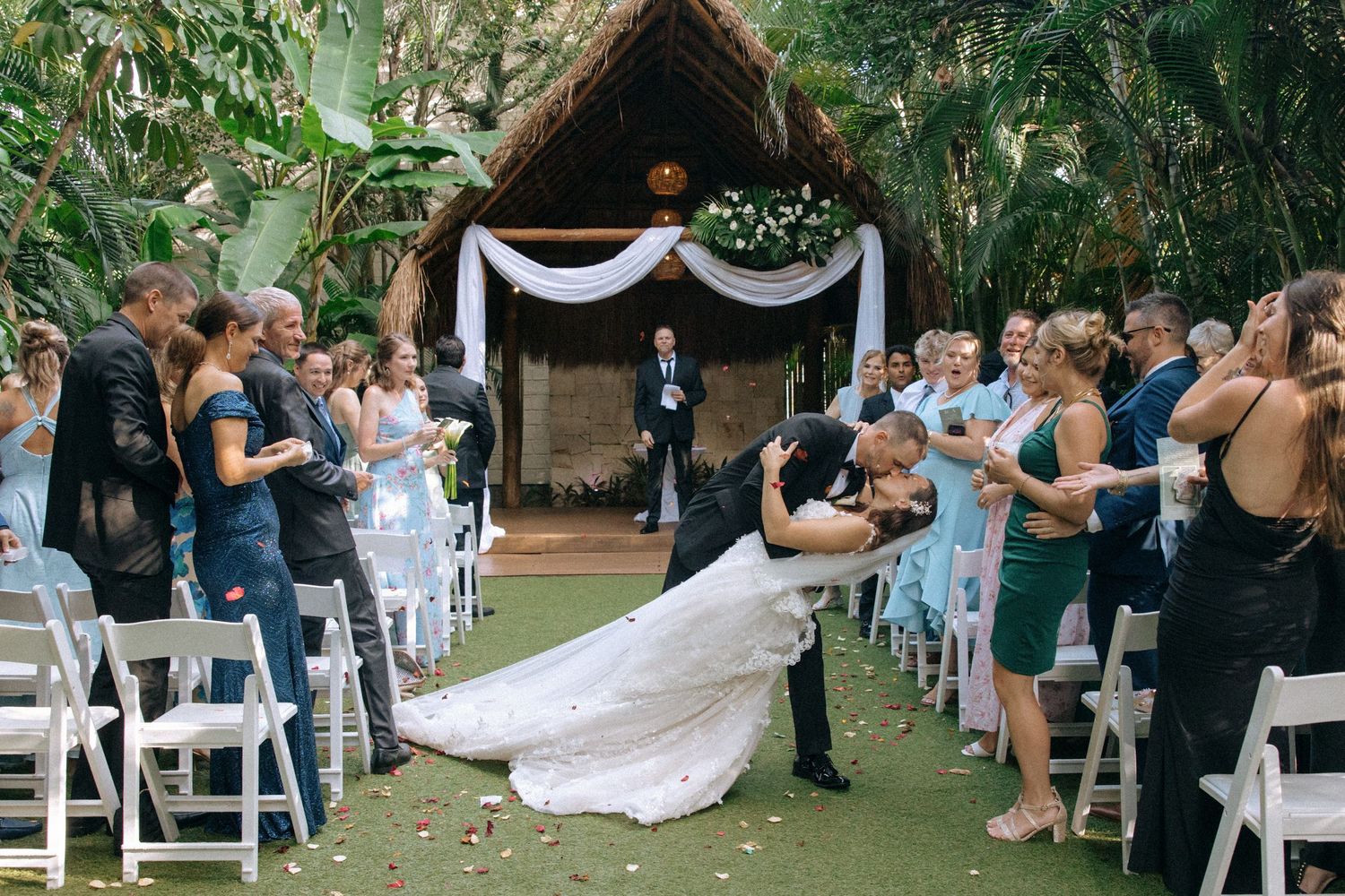 Outdoor wedding ceremony setup with rows of white chairs and decorative fabric draping in a lush garden setting.