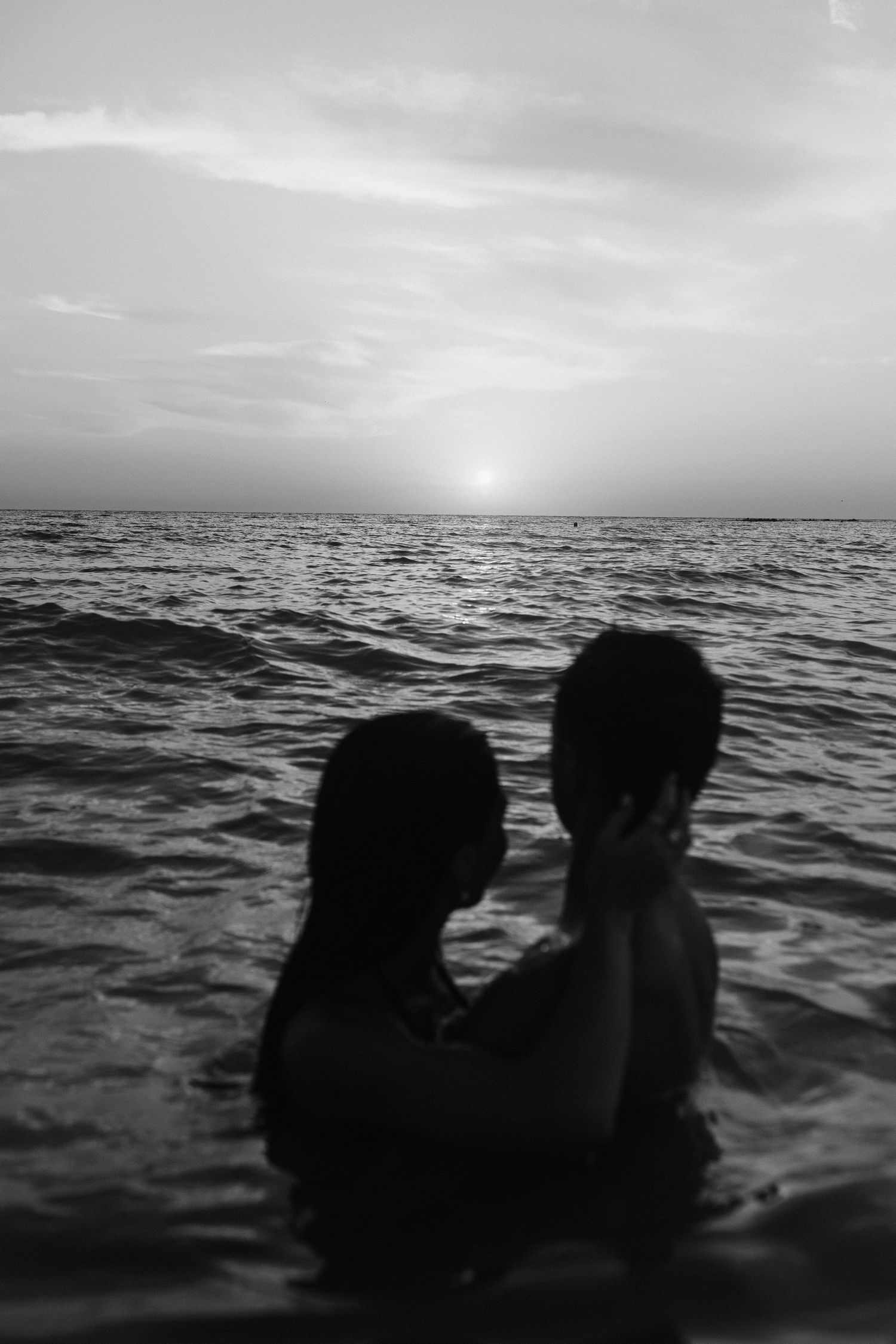 Two silhouettes embrace in dark waters against a moody ocean horizon.