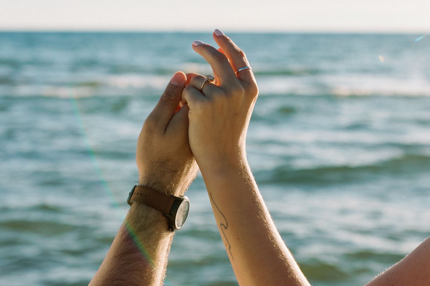 Raised hands against a blurred ocean background at sunset.
